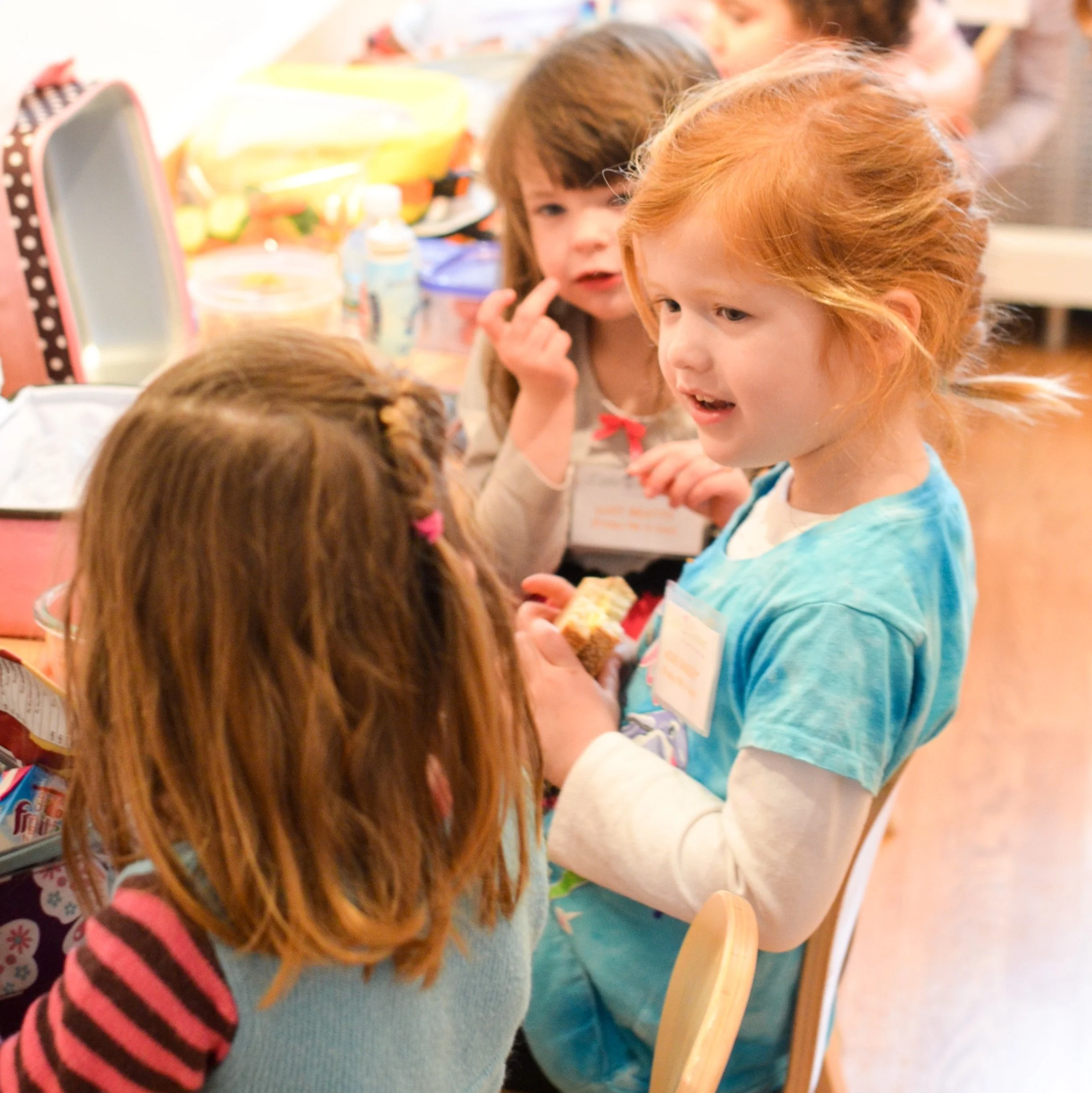 Children talking and sharing a snack in a classroom or daycare setting.