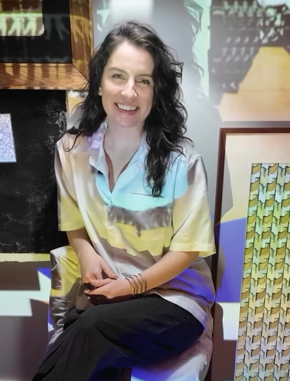A woman sitting and smiling in front of a colorful background.
