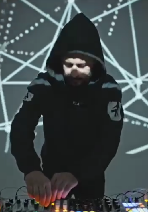 Person wearing a hoodie DJing with a digital music mixer, abstract geometric light patterns in the background.