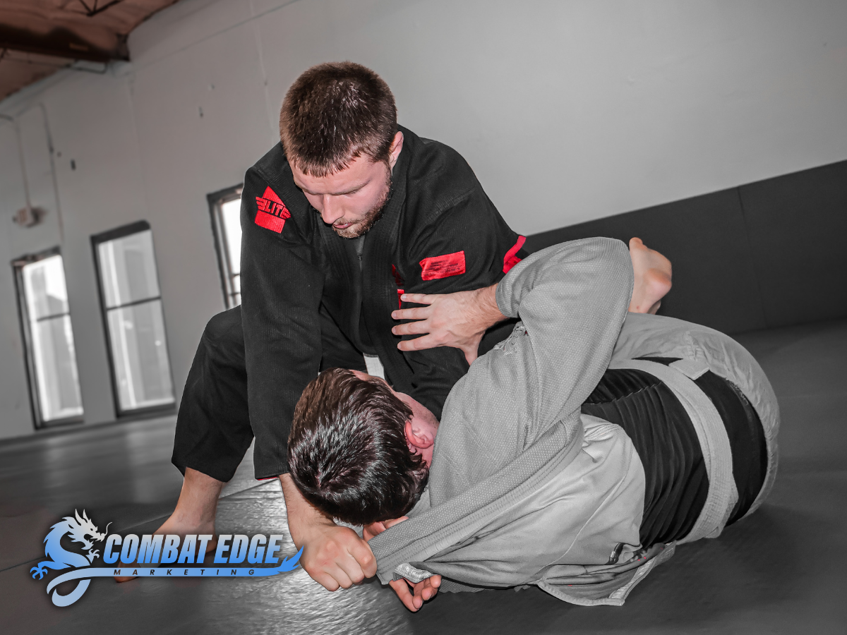 Two men practicing Brazilian Jiu-Jitsu on a black mat, with one applying a chokehold on the other in a martial arts training facility.