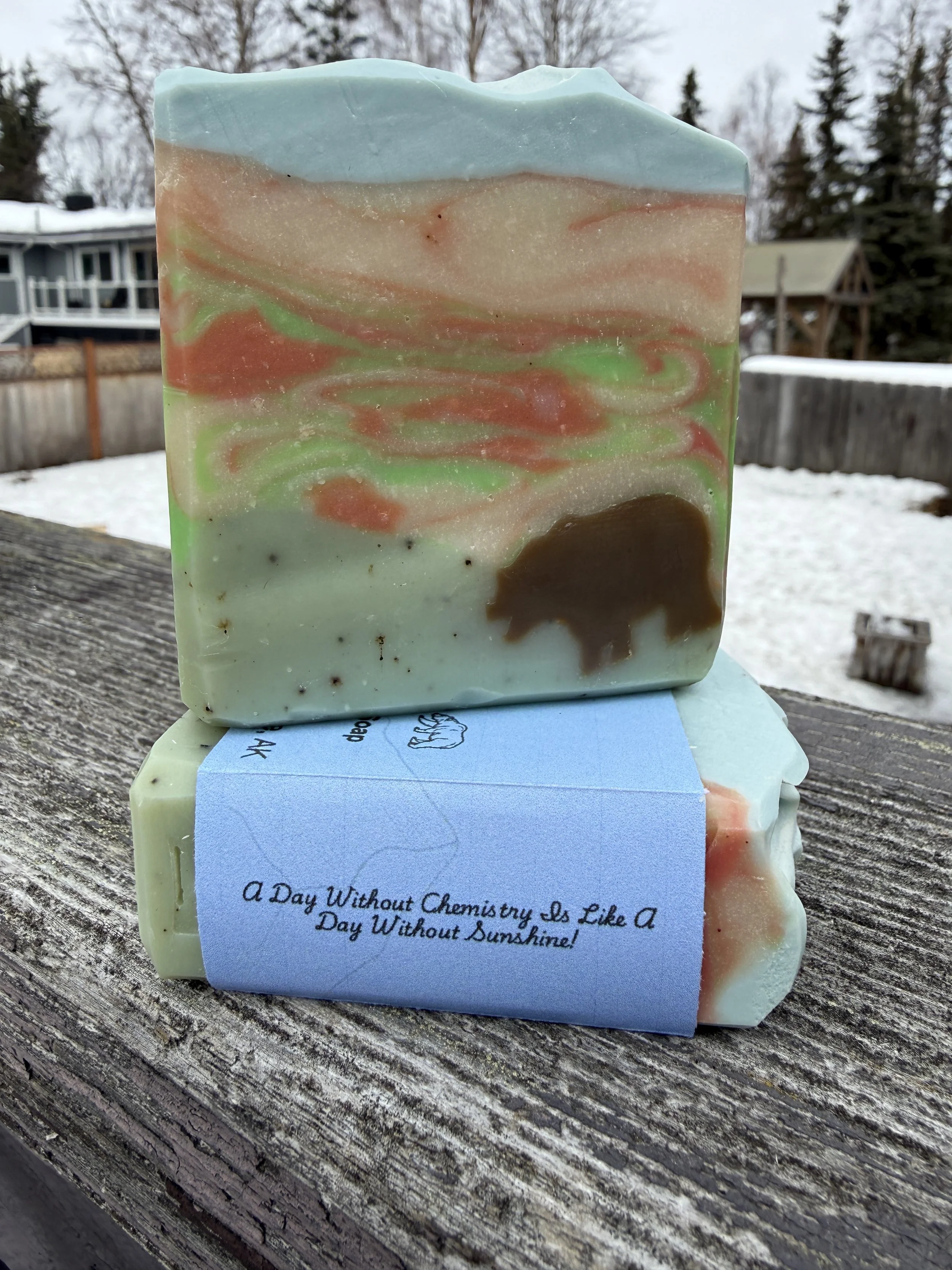 Handcrafted Tundra soap with bear embed, featuring green and earthy swirls, displayed outdoors on a wooden surface with snow in the background