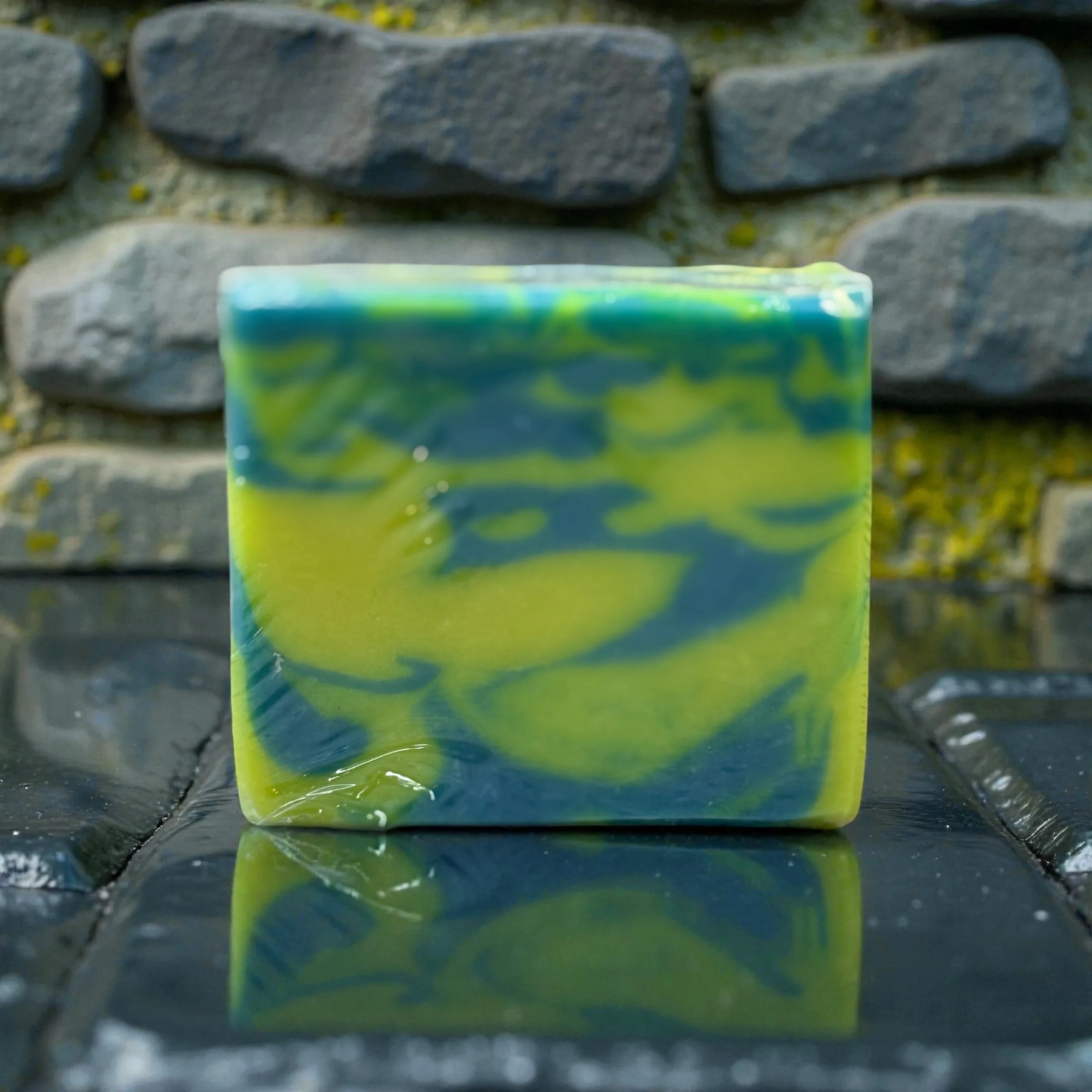 Square bar of green and yellow swirled soap against a stone backdrop.
