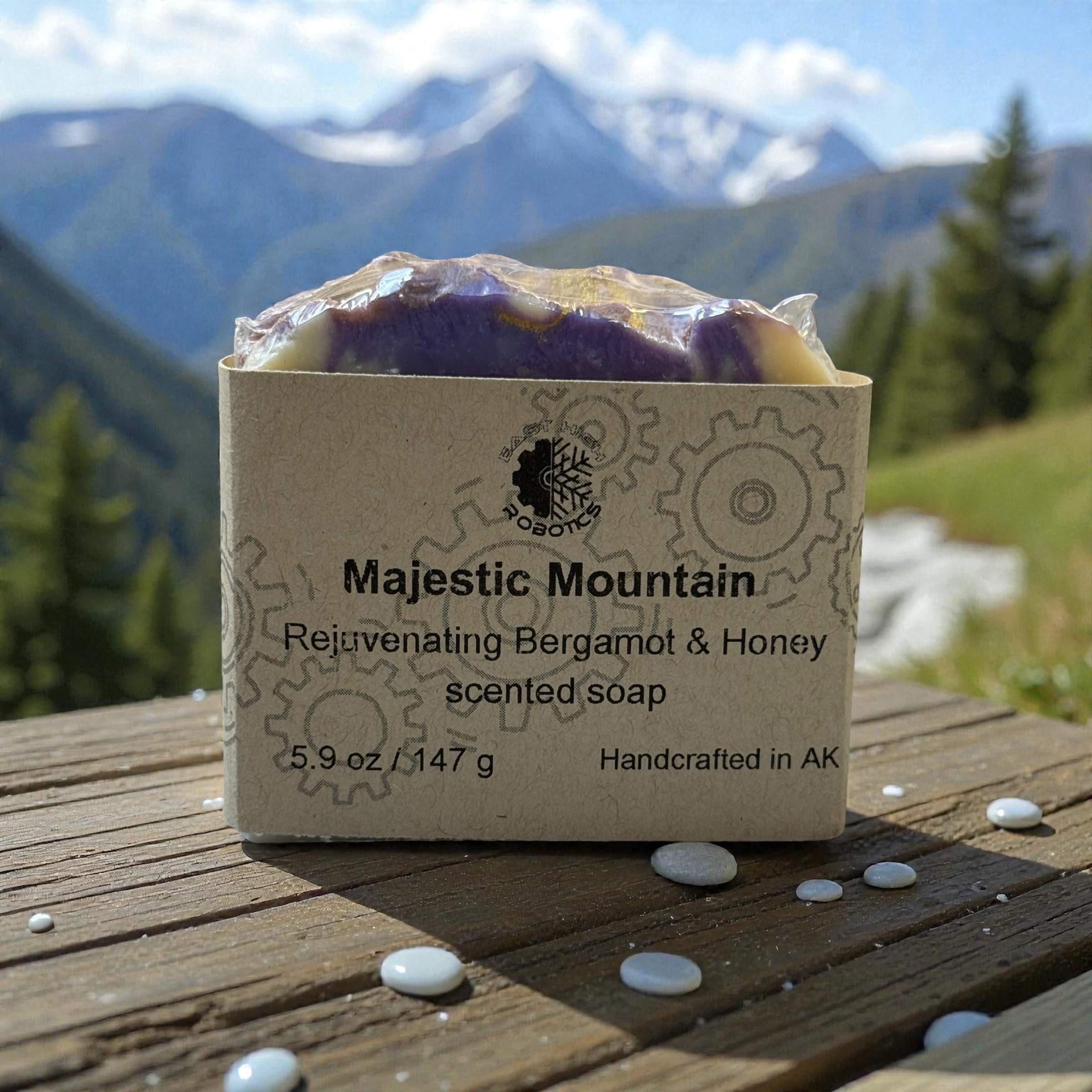 A single bar of soap wrapped in brown paper with the text Majestic Mountain. The soap is sitting on a railing with mountains in the background. The top of the soap is purple.