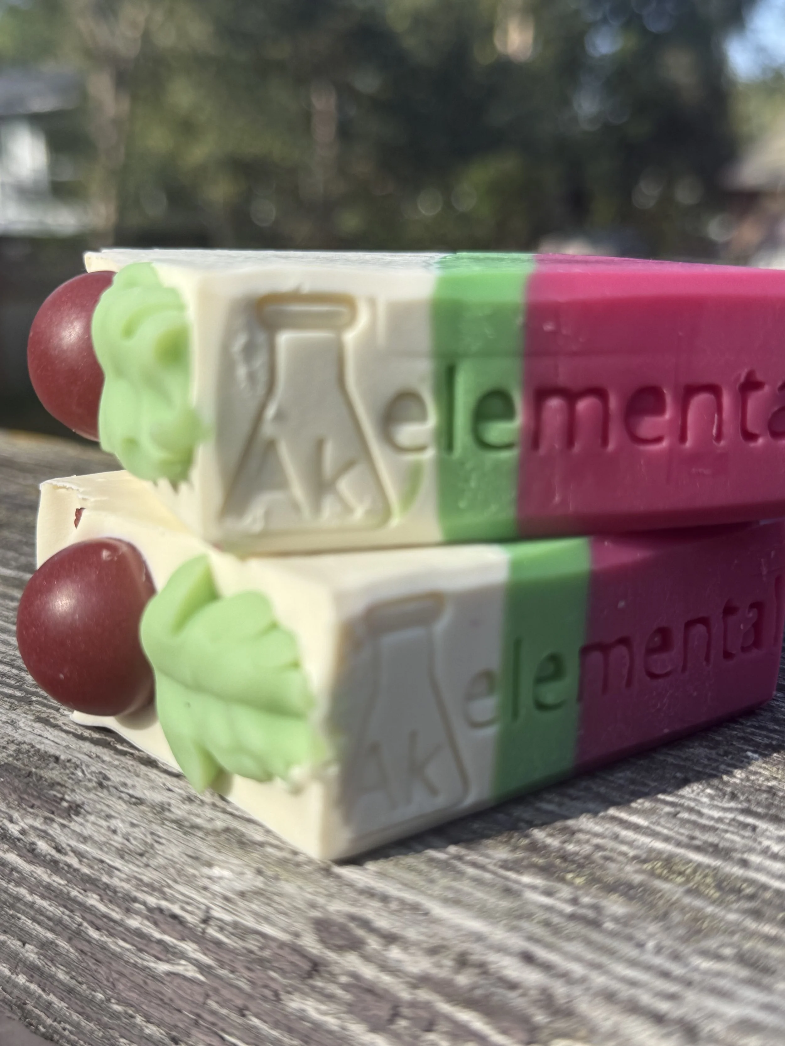 Side view of two Handcrafted Wild Cranberry soap bars with cream, evergreen green and cranberry red diagonal layers and festive round soap embeds on top.