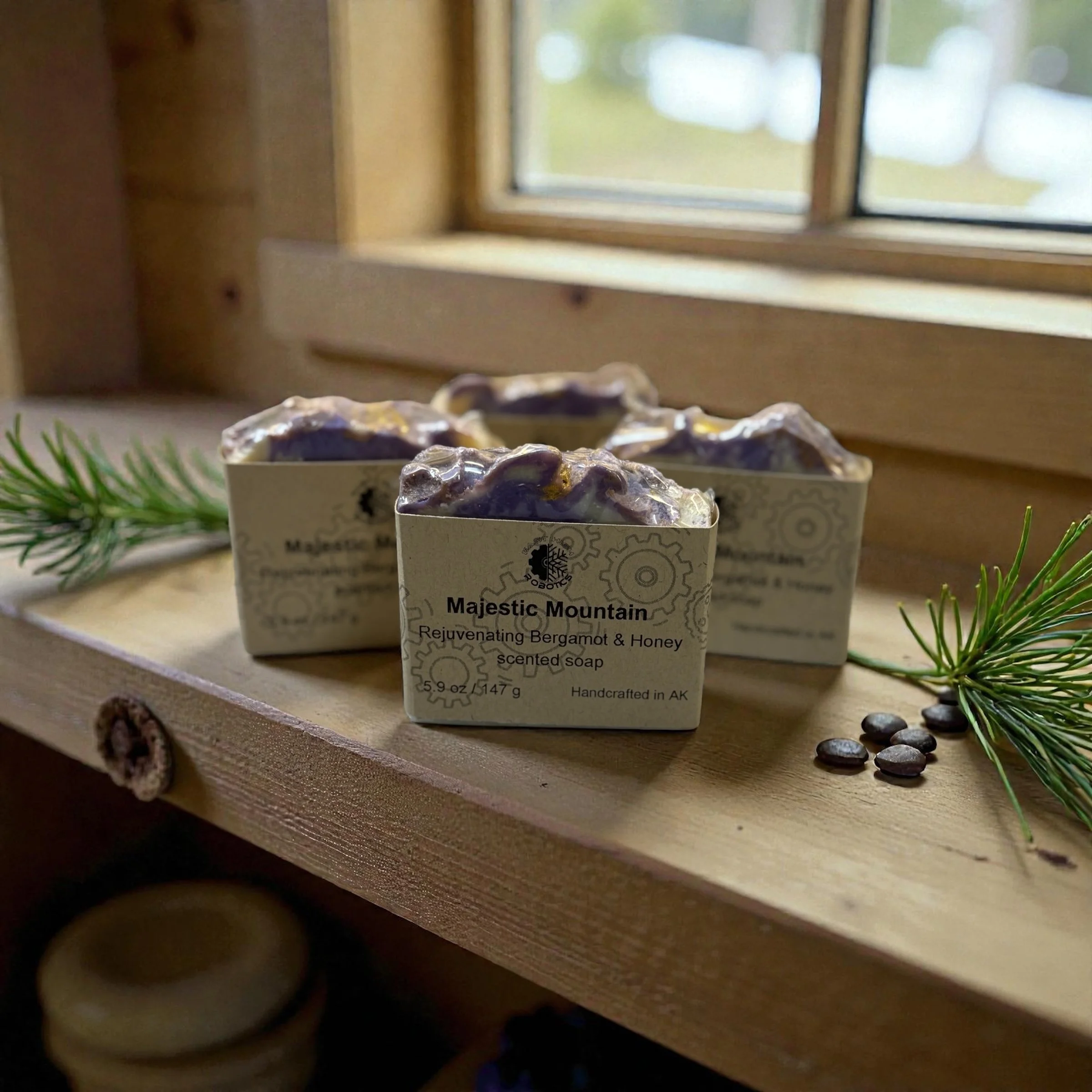 Three bars of soap sitting on a wooden shelf in front of a window. Text on brown label reads Majestic Mountain.