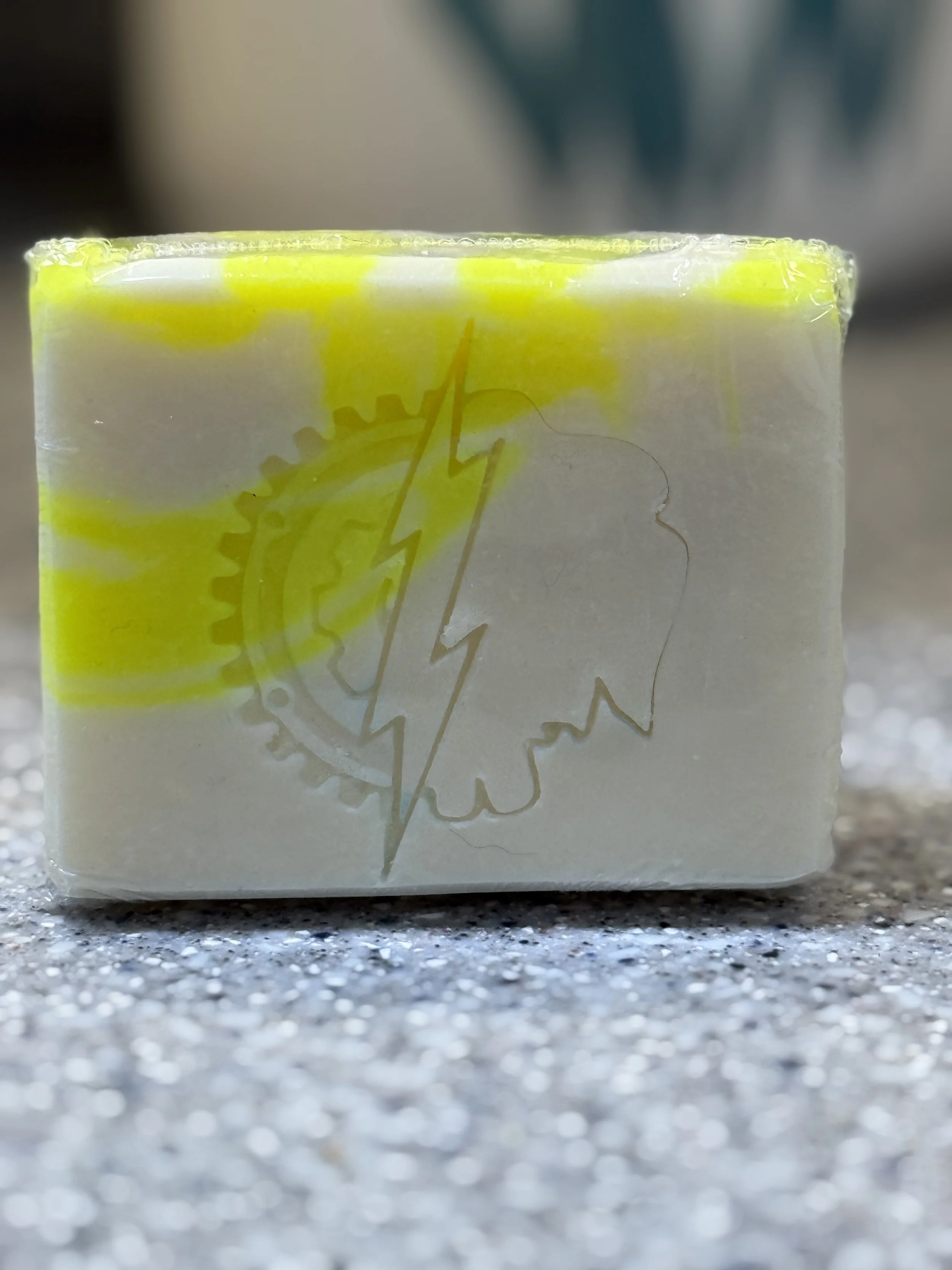 Yellow handcrafted soap with yellow and white swirls. Lightning bolt stamp on front of soap.
