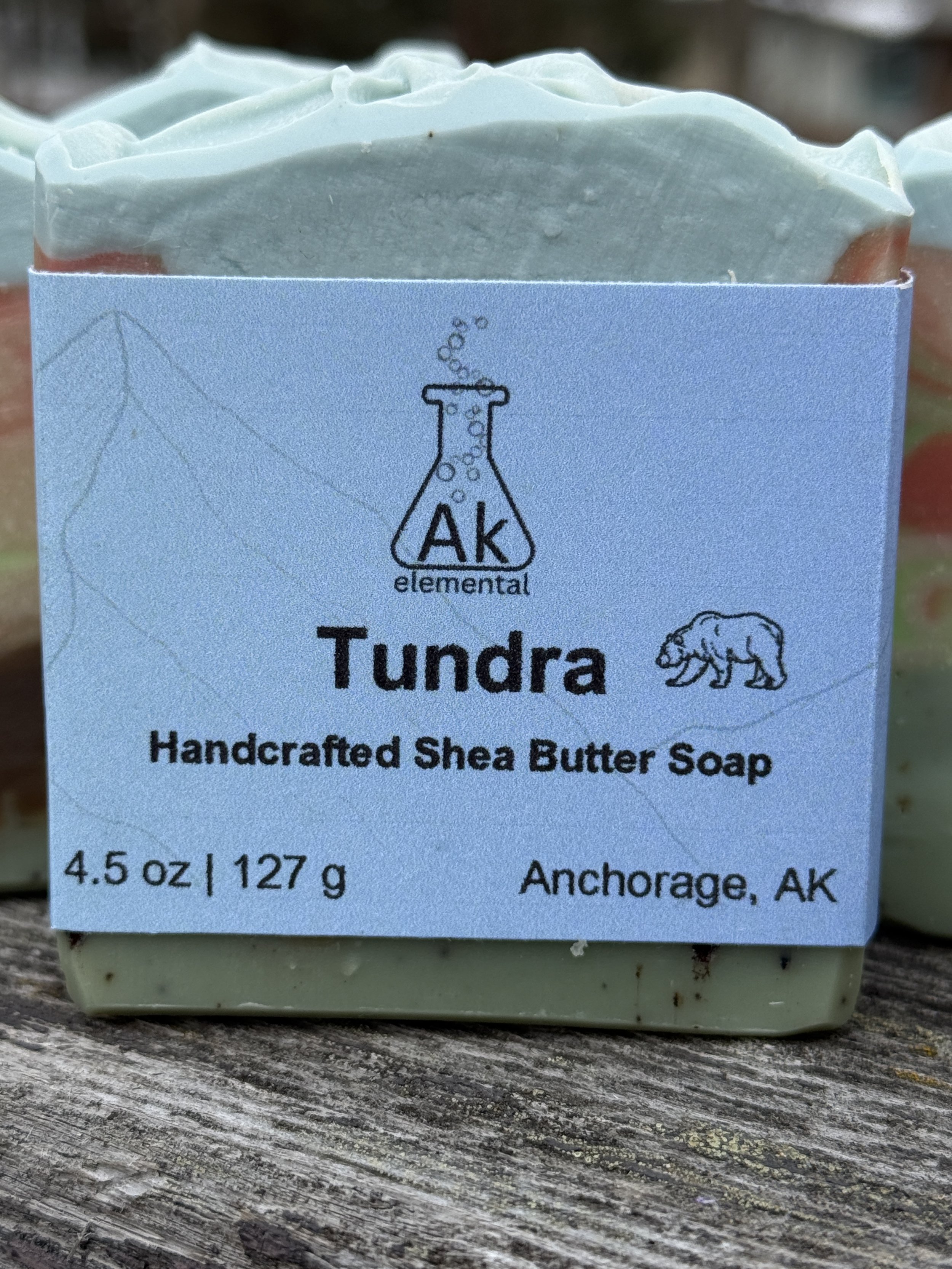 Rectangular soap bar with avocado oil, coconut milk, and bear embed, styled outdoors in snowy Alaska setting