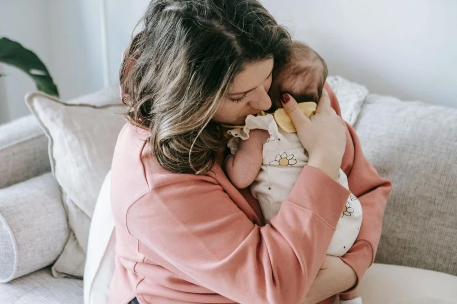 A woman in a peach sweater gently holds a baby, symbolizing the postpartum depression awareness color