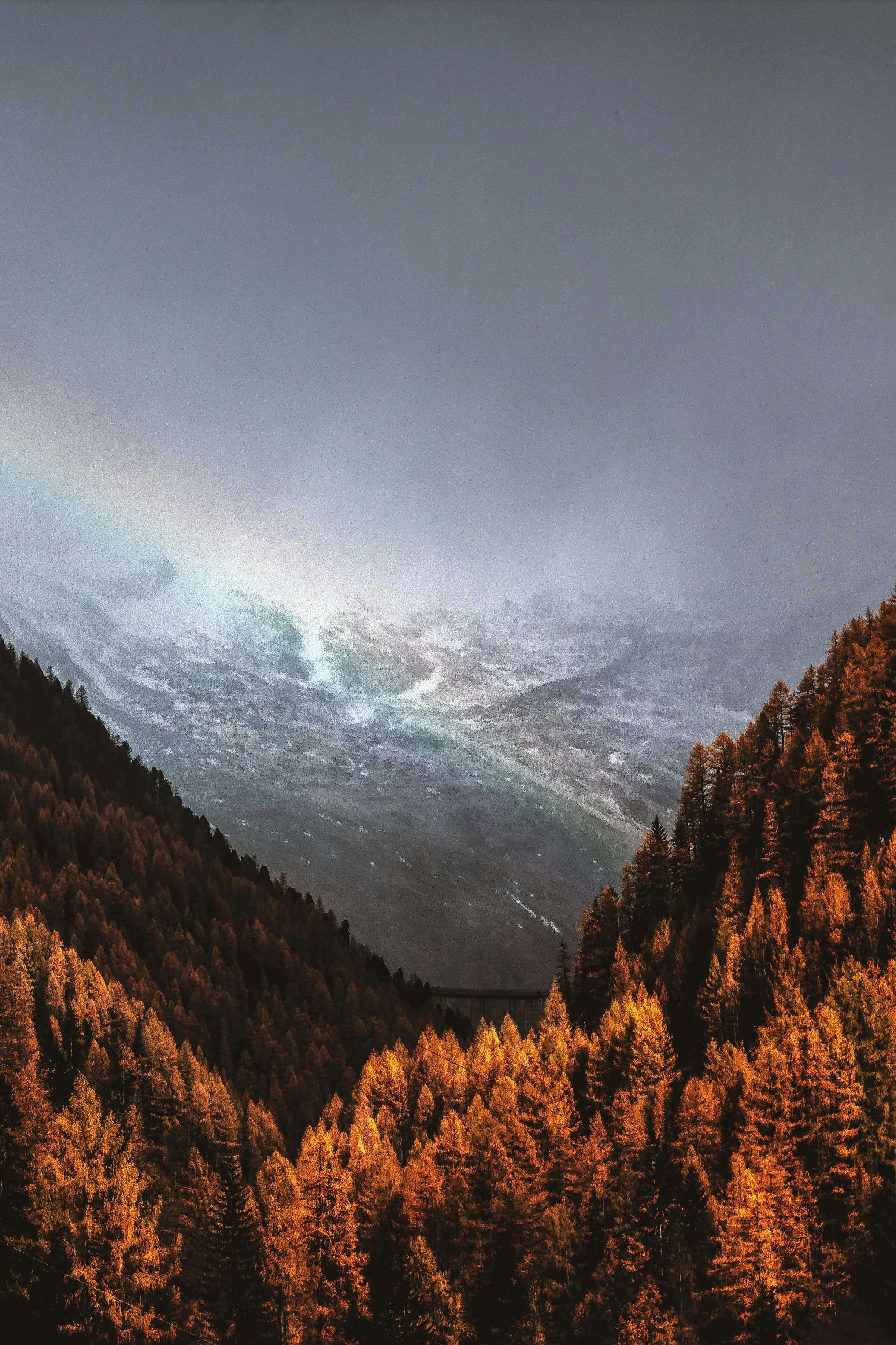 Mountain landscape with colorful autumn trees on hills and a rainbow in the cloudy sky.