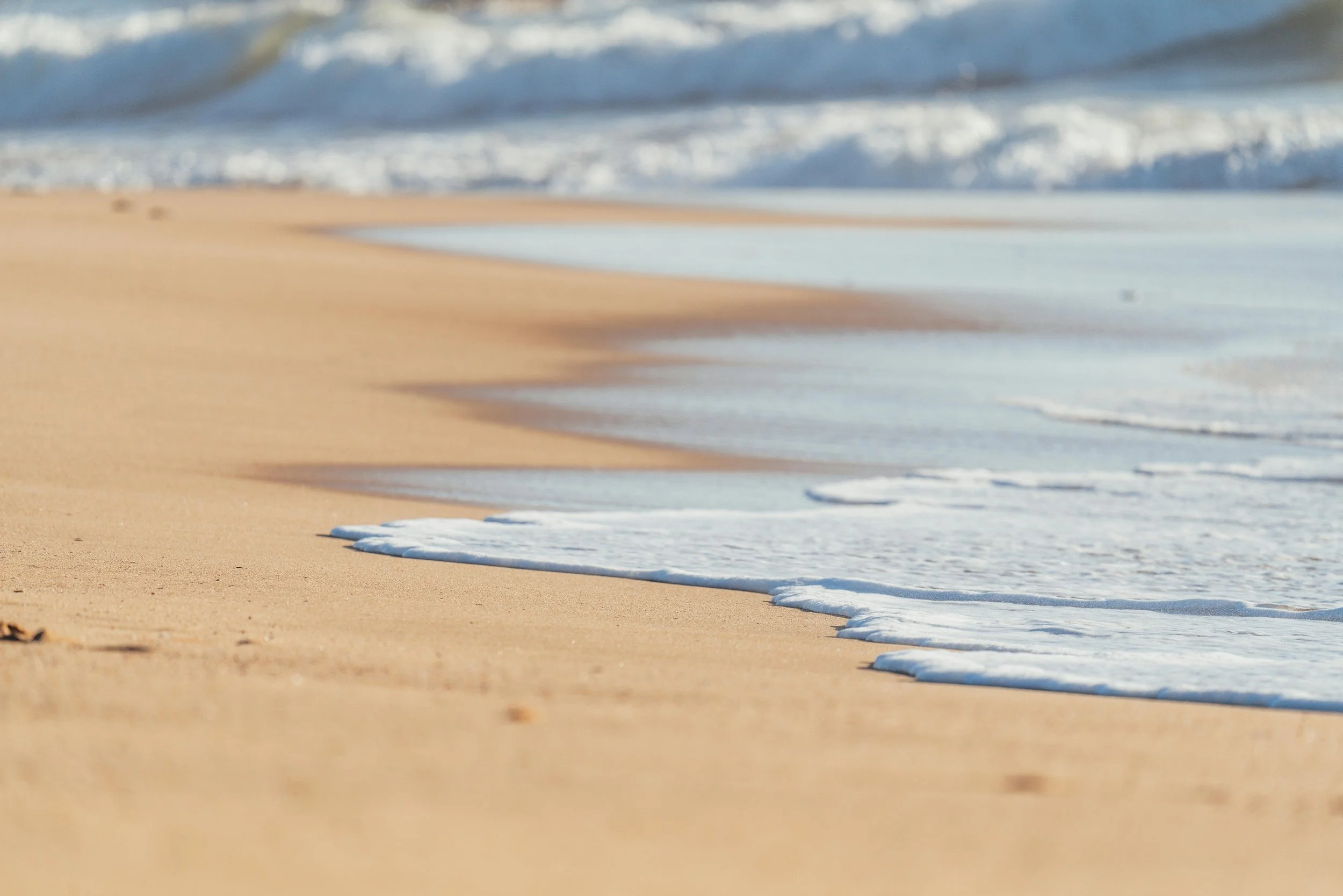 Close-up view of gentle waves washing onto a sandy beach.