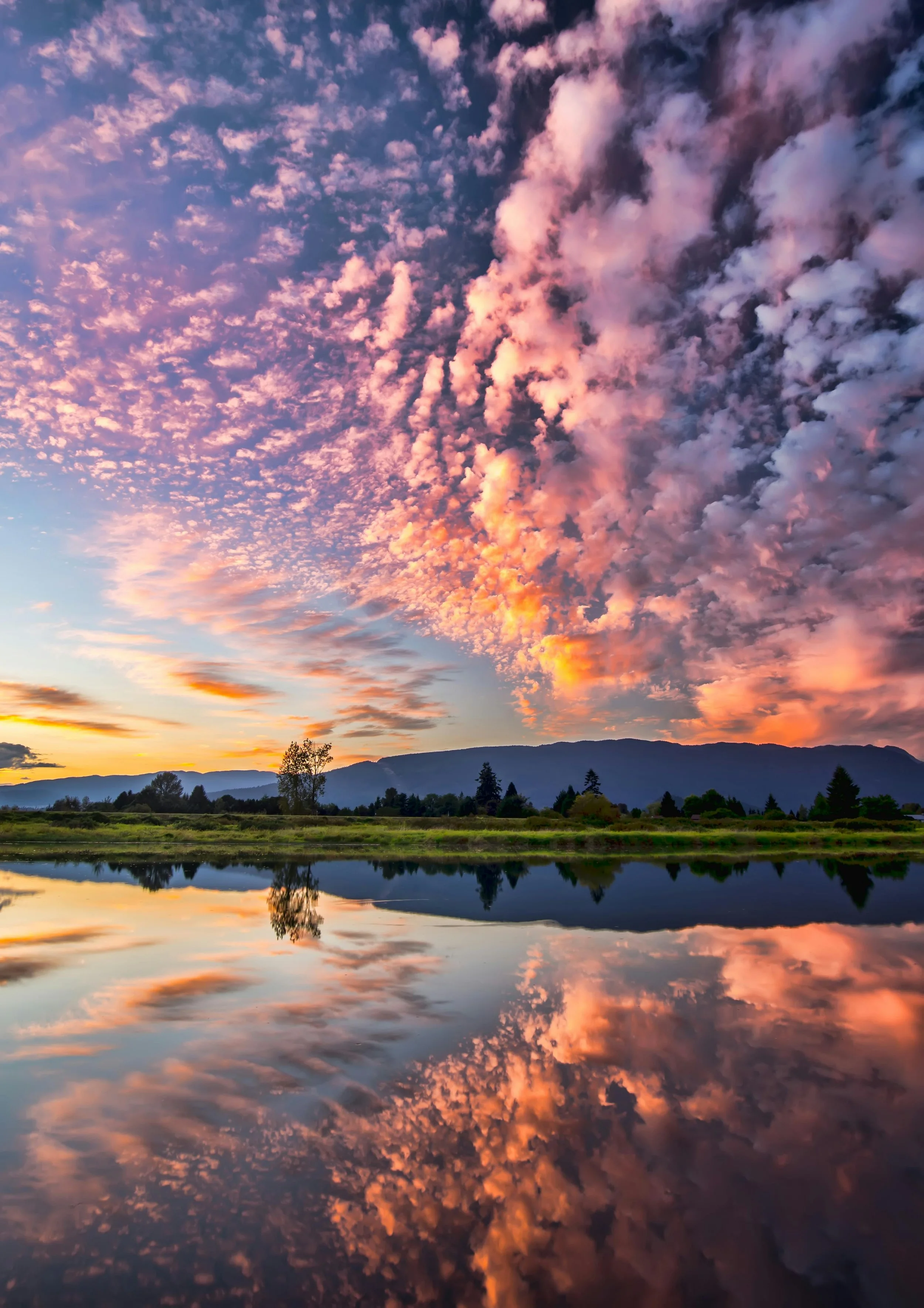 Sunset over a lake with colorful clouds and mountains in the background, reflected in the water.