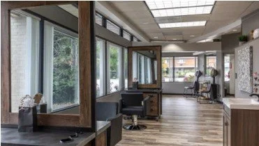 Empty hair salon with large windows, styling stations, mirrors, and chairs