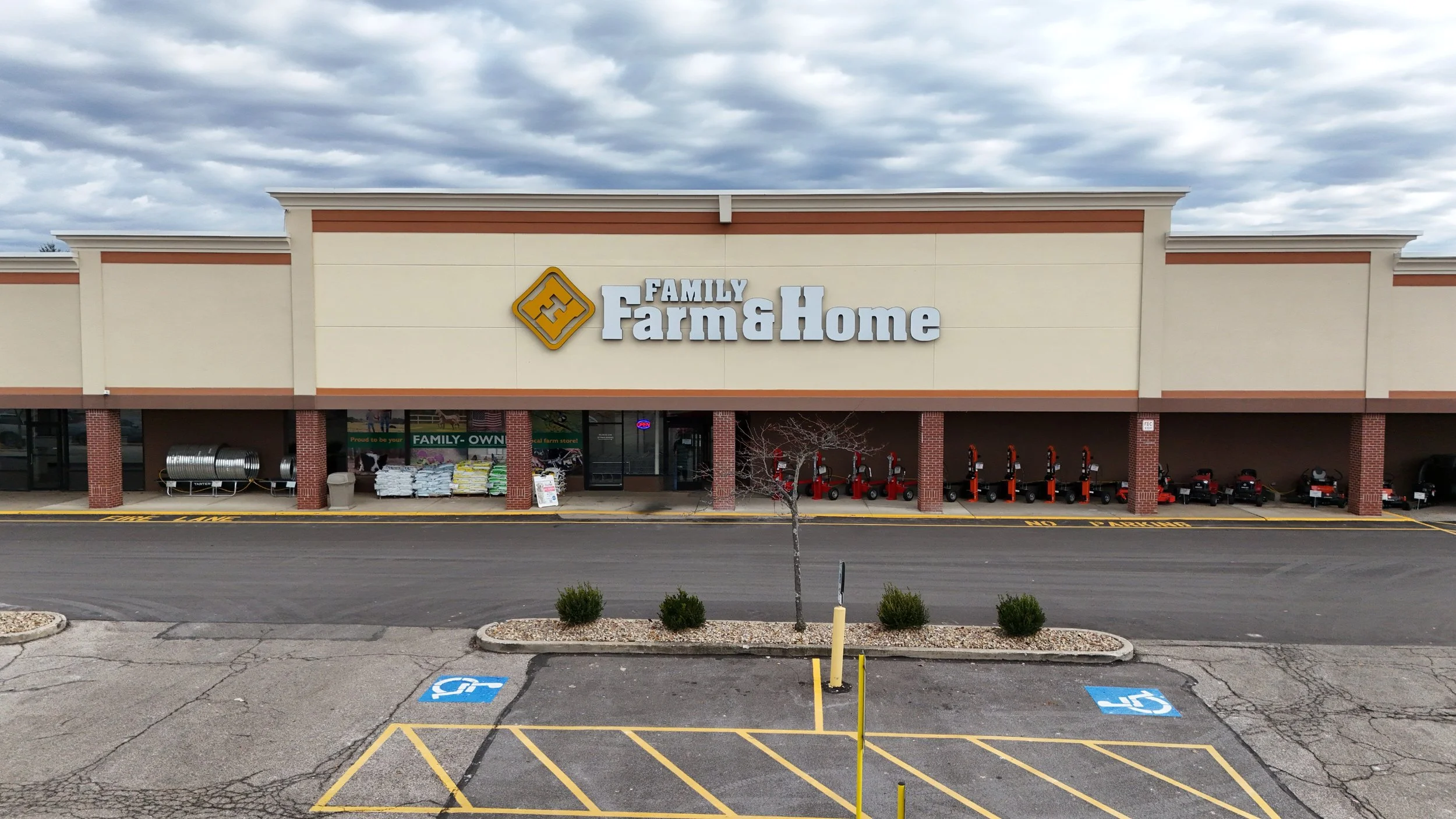 An empty shopping plaza with a large sign on the building that reads "Coming Soon." The store sign says "The Family Farm & Home." The sky is partly cloudy.
