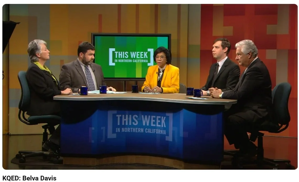 Television talk show set with five people seated around a curved desk, a woman in a yellow blazer speaking, and a large screen behind displaying "This Week in Northern California".