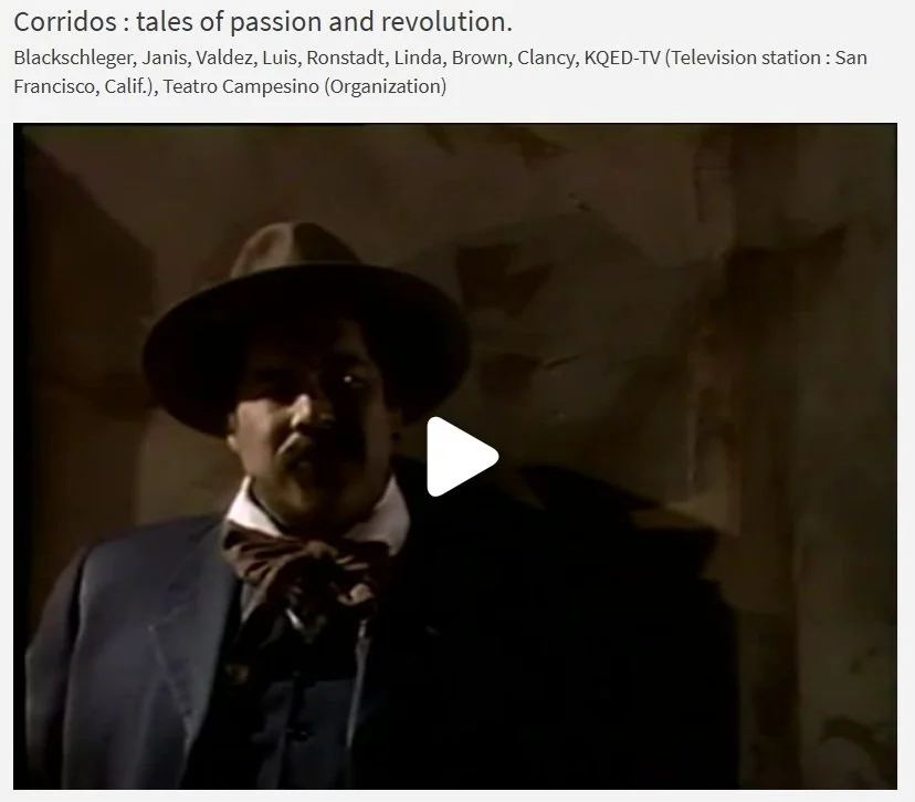 A man dressed in old-fashioned clothing, wearing a wide-brimmed hat, standing in a dimly lit room with a rough, textured wall in the background.