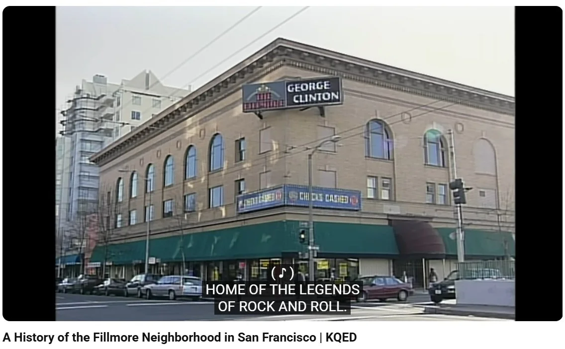 An urban street scene in San Francisco featuring a historic building with a marquee and electronic sign promoting George Clinton, with parked cars and a traffic light, under cloudy skies.