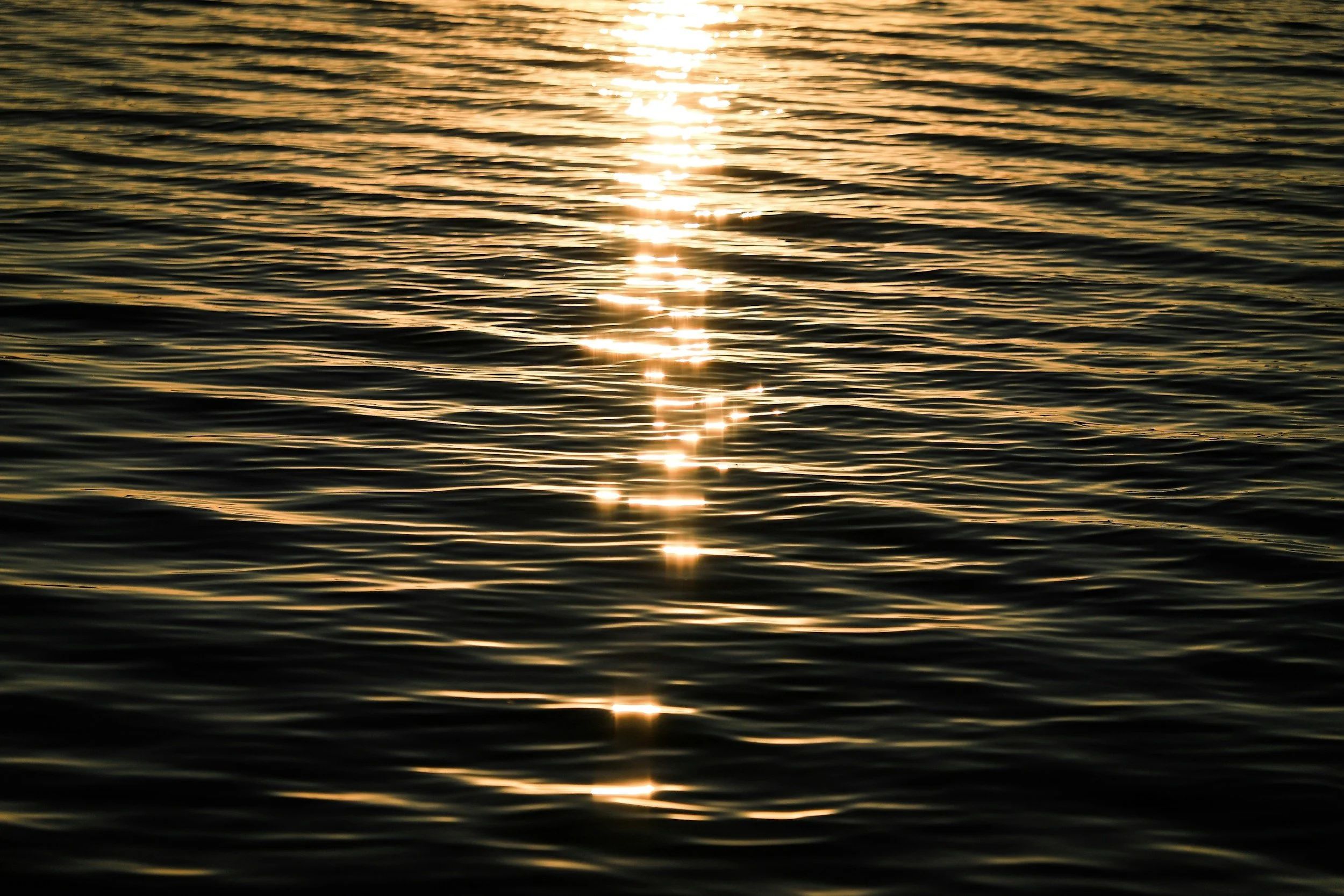 Sunset reflecting off calm ocean water with gentle ripples.
