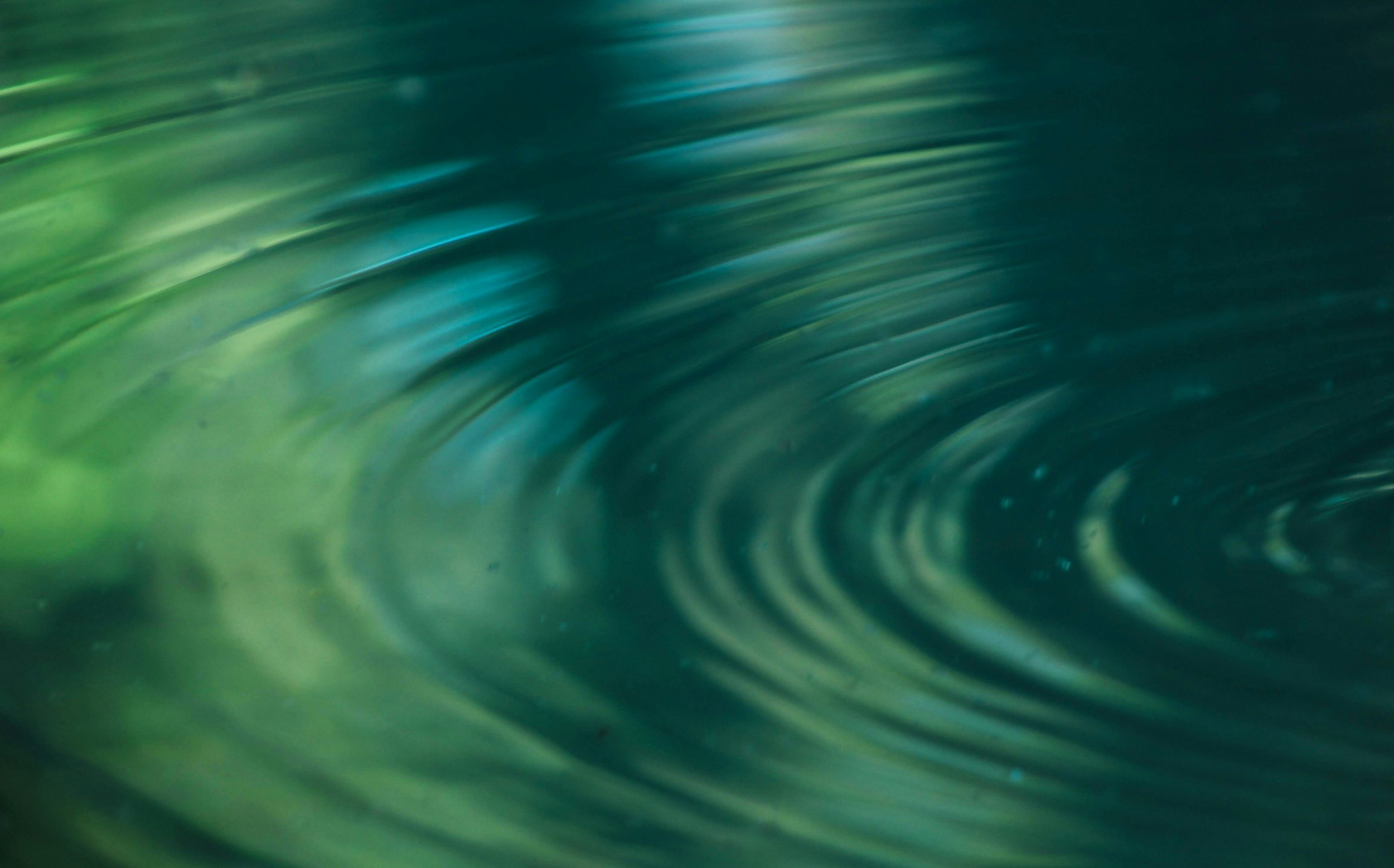 Close-up image of swirling water with green and blue hues creating a wave-like pattern.