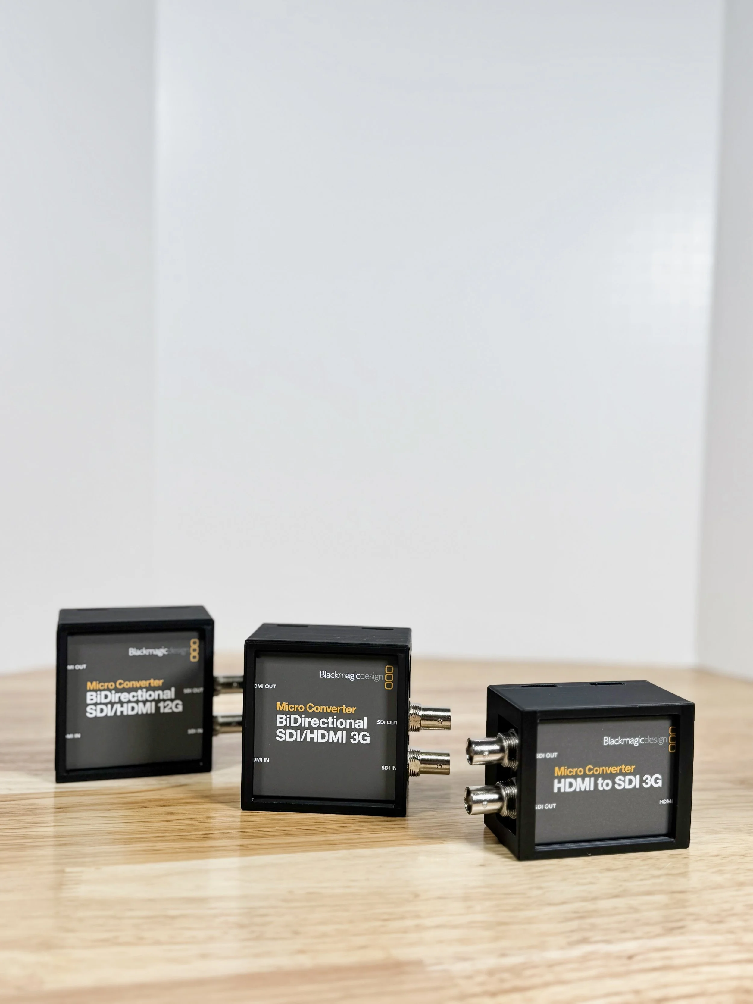 Three black electronic video signal converters on a wooden surface, labeled for SDI/HDMI conversion, with two connected together and one separate.