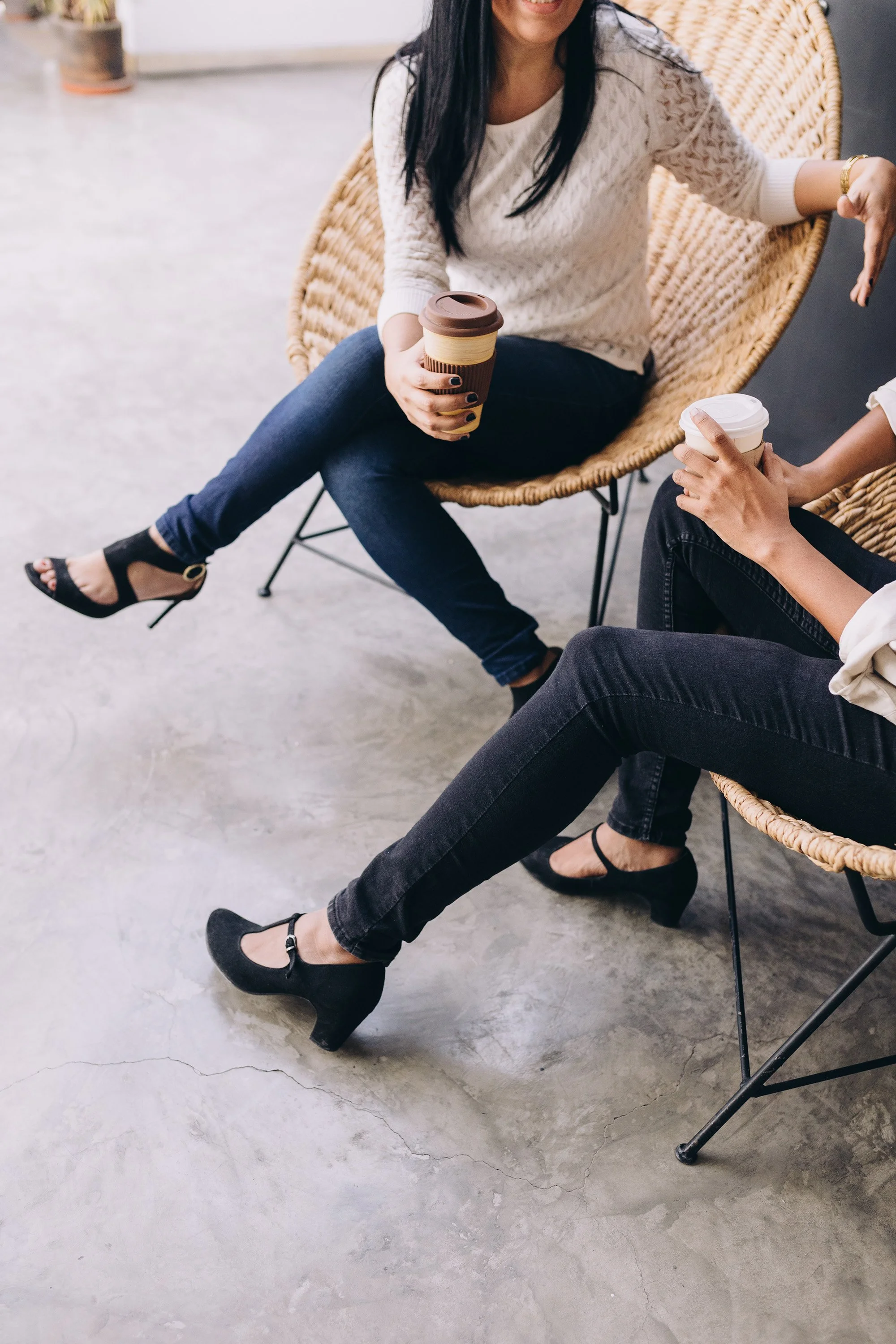 Two women sitting in wicker chairs having a conversation, holding coffee cups.