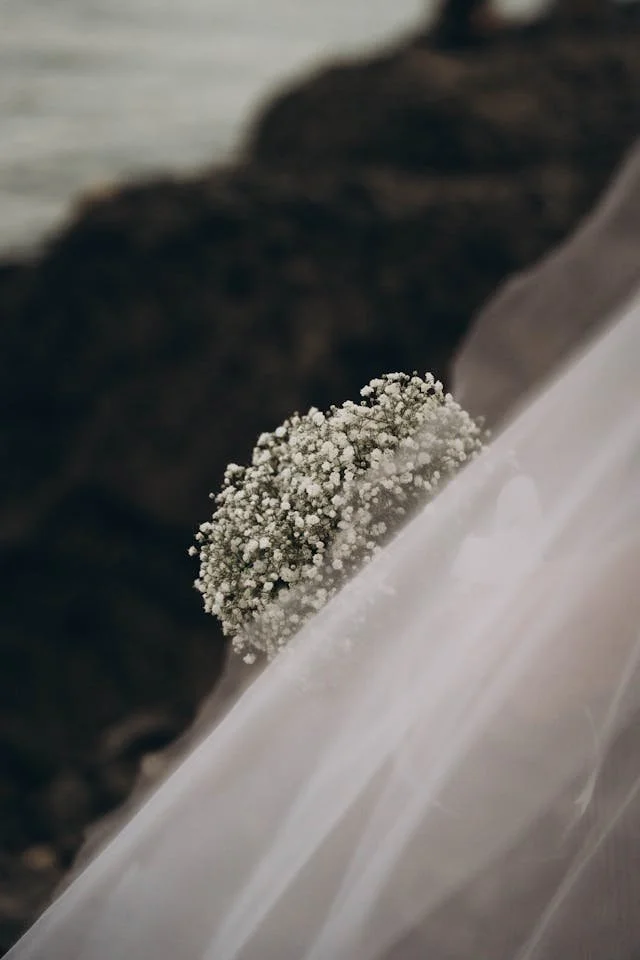 A close-up of a white wedding dress with lace and a small white bouquet of baby's breath flowers on the skirt.