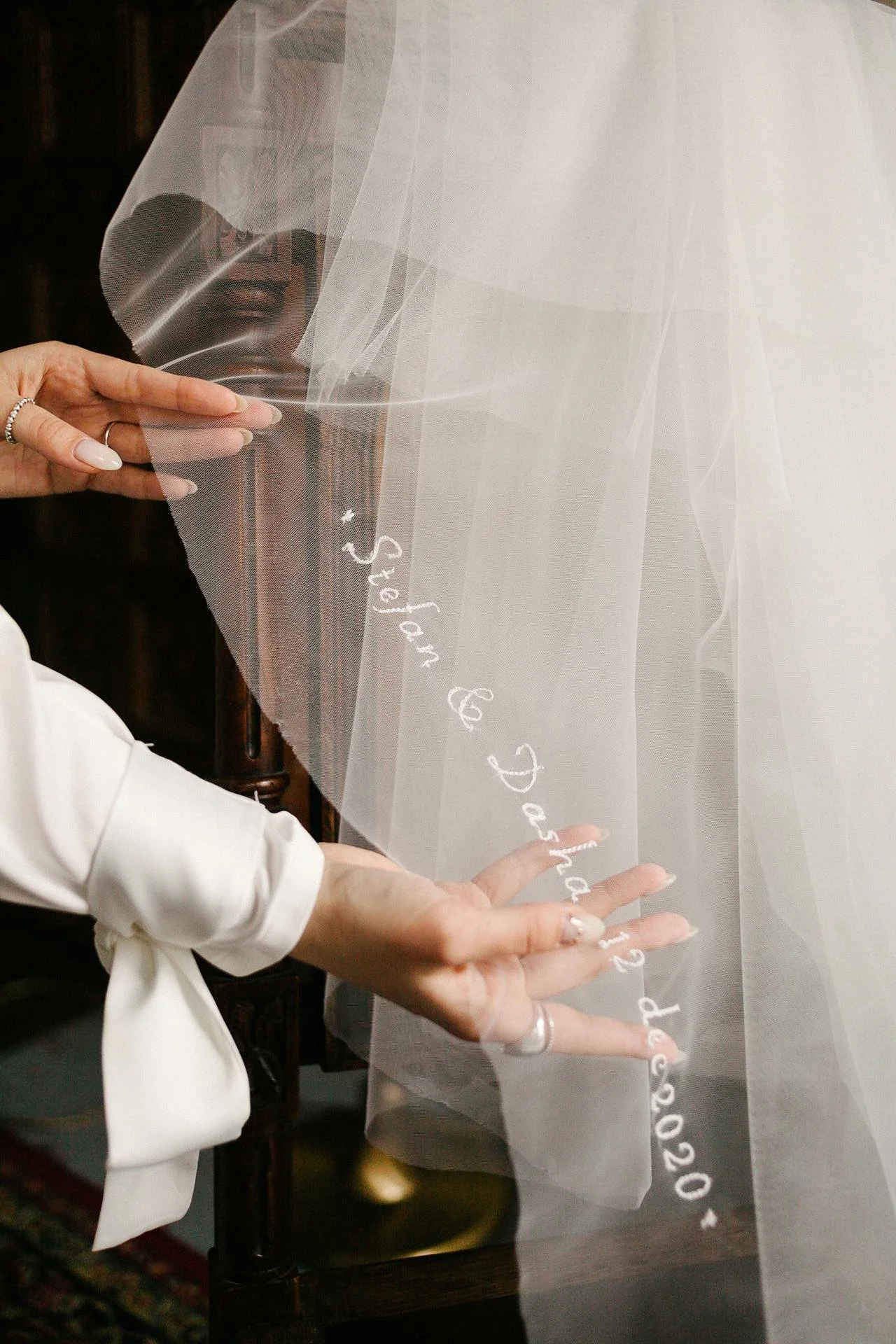 A person with manicured nails holds a sheer veil with white embroidered text that reads 'You & Me Since 2020'.