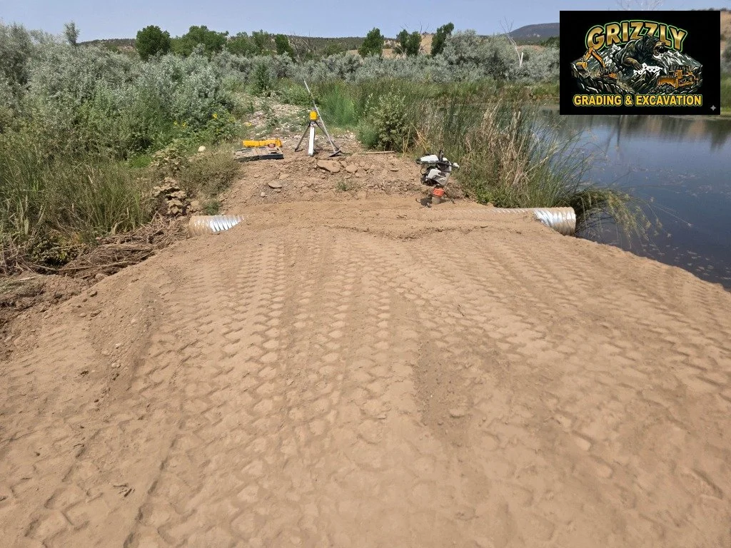 The overflow on this pond near Midway washed out. Grizzly came in to do it right &mdash; CMP pipe set, bedding compacted, approach laser graded. When the water comes up next spring, it goes where it's supposed to. This is the kind of fix that doesn't