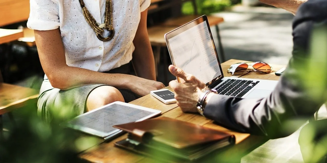 People having a business meeting with laptops, notebooks, sunglasses, and a tablet on a wooden table. Researching the most optimal and best ways to improve your business.