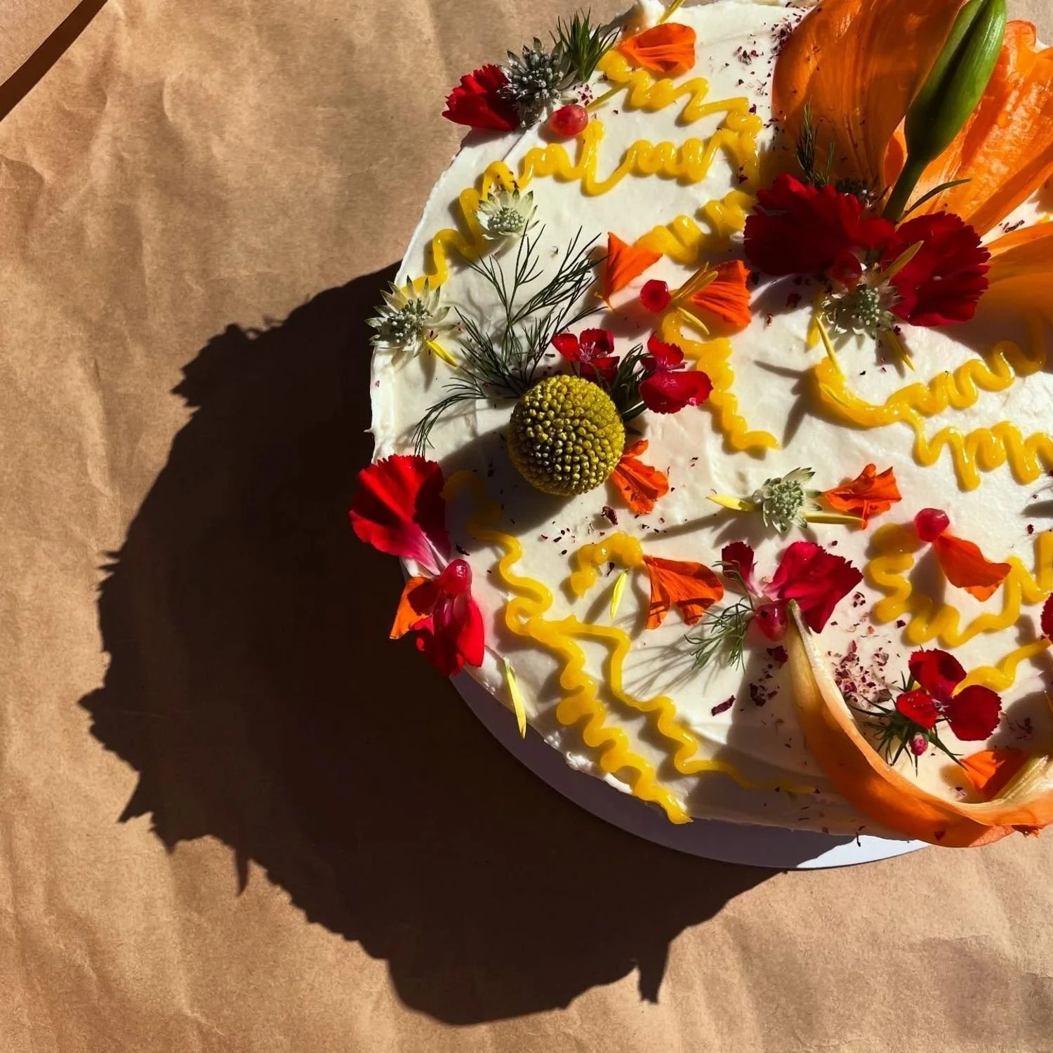 Decorated birthday cake with colorful flowers, yellow icing, and a candle on top.