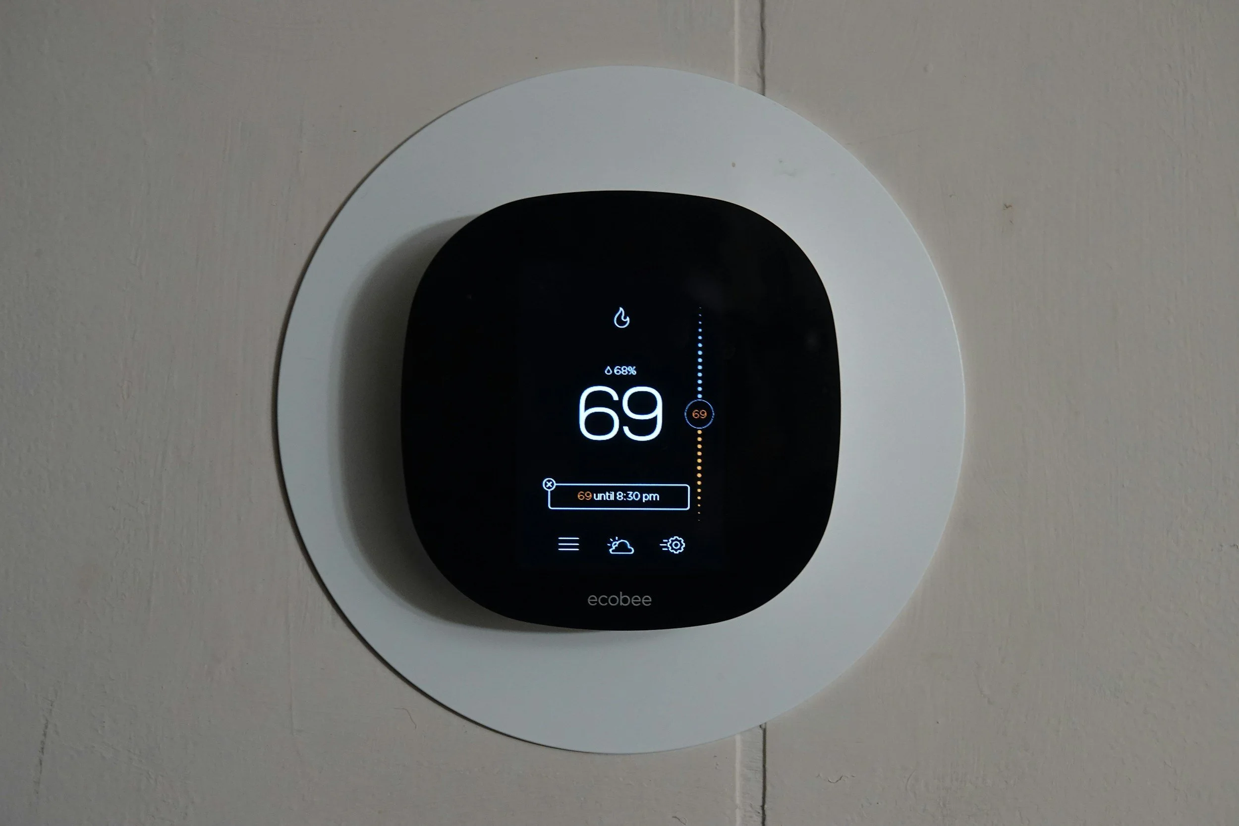 A circular smart thermostat mounted on a wall, displaying the temperature of 69 degrees Fahrenheit, with the background wall being beige or light gray.