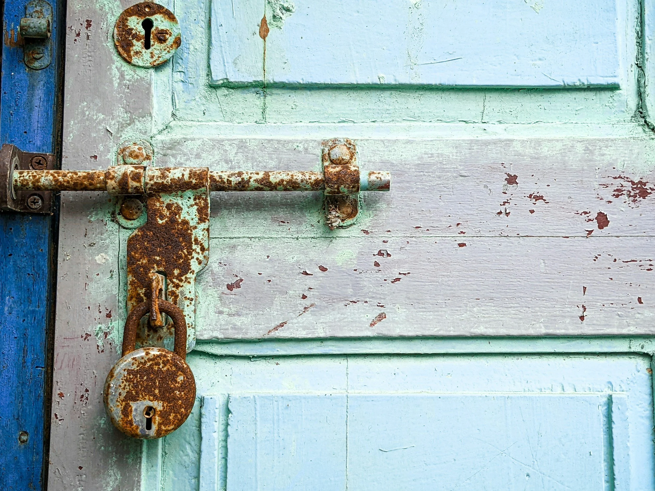 A close-up of an old, rusty iron latch and lock on a weathered light blue wooden door.