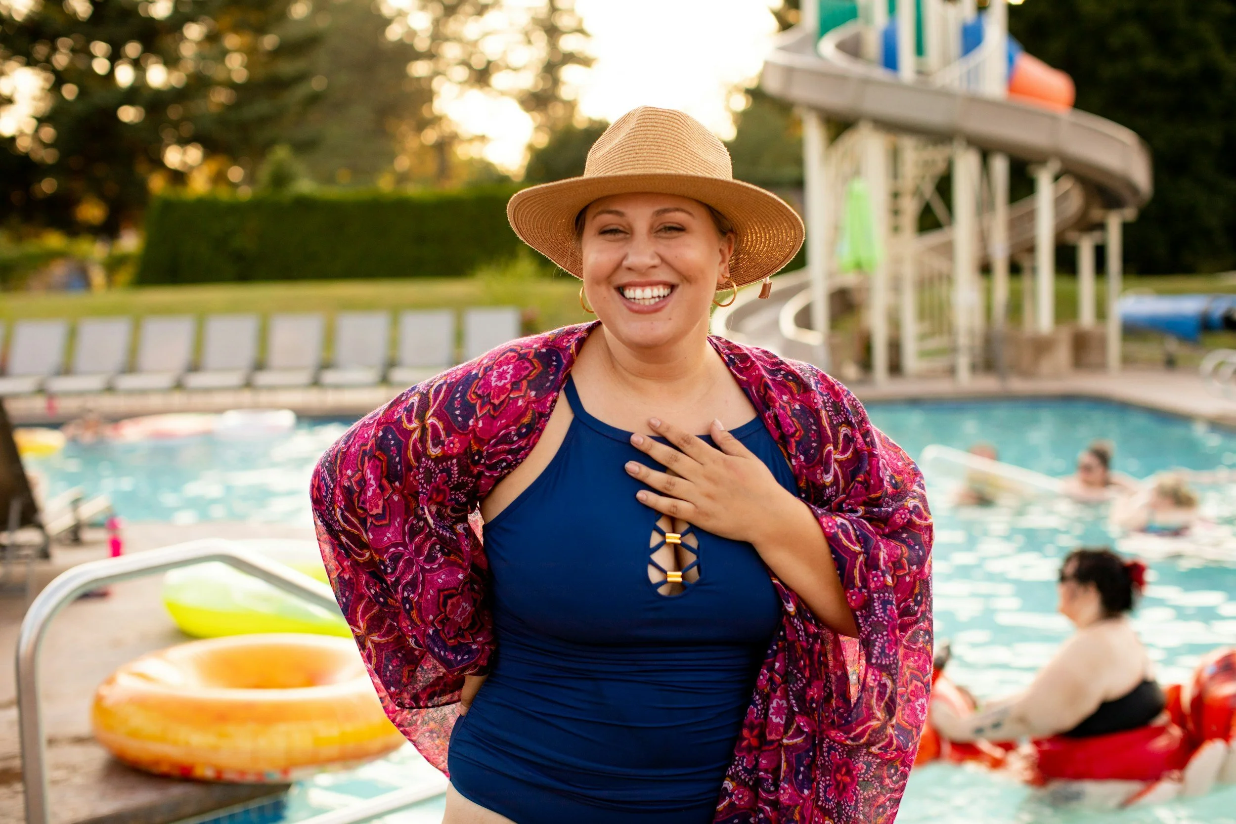 Smiling woman in swimsuit and wide-brimmed hat at a summer pool party.