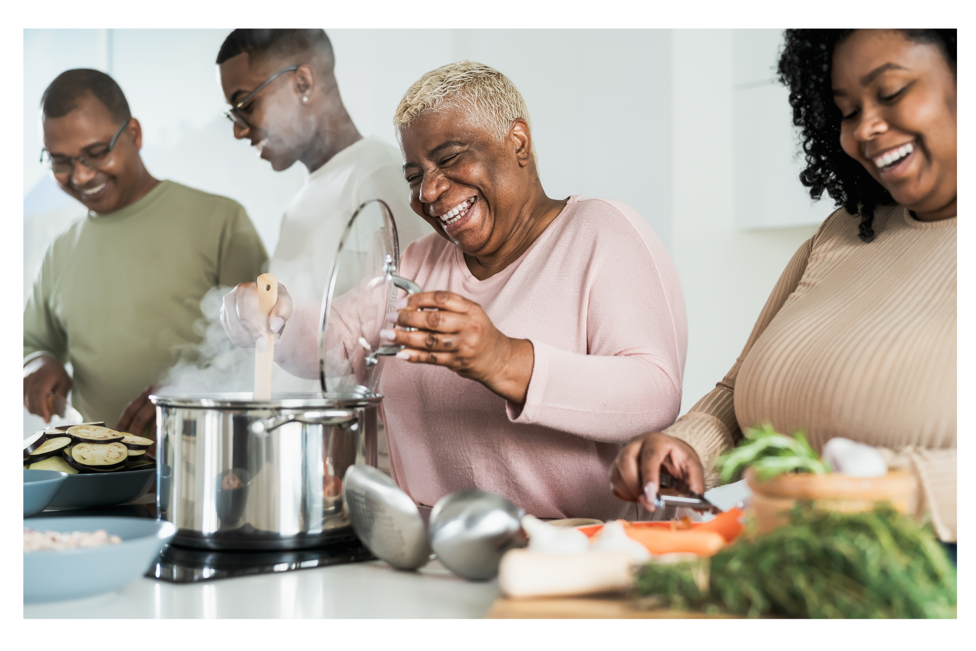 An African American family of four cooking and preparing food in a bright kitchen, smiling and enjoying the activity.