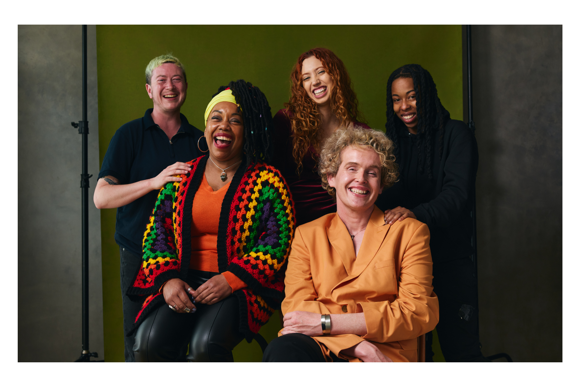 Group of five diverse women laughing and smiling in a photography studio with a green and gray background.