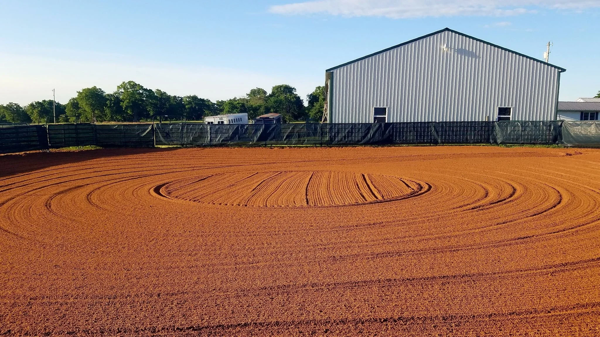 A cutting pen arena, with a large metal building and green trees in the background under a clear blue sky.