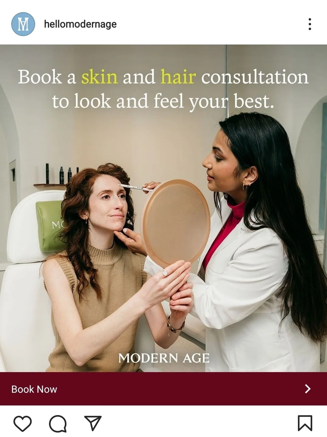 A woman with curly brown hair sitting in a chair, receiving a skin treatment from a female dermatologist with long black hair. The dermatologist is holding a mirror and examining the woman's face.