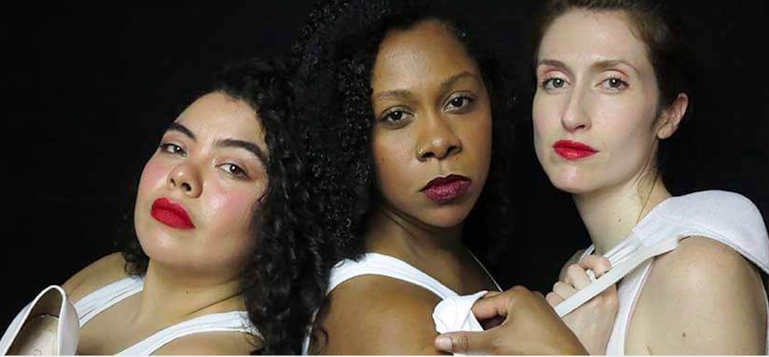 Three women with different skin tones and hair types posing against a black background, wearing white tops with serious expressions.