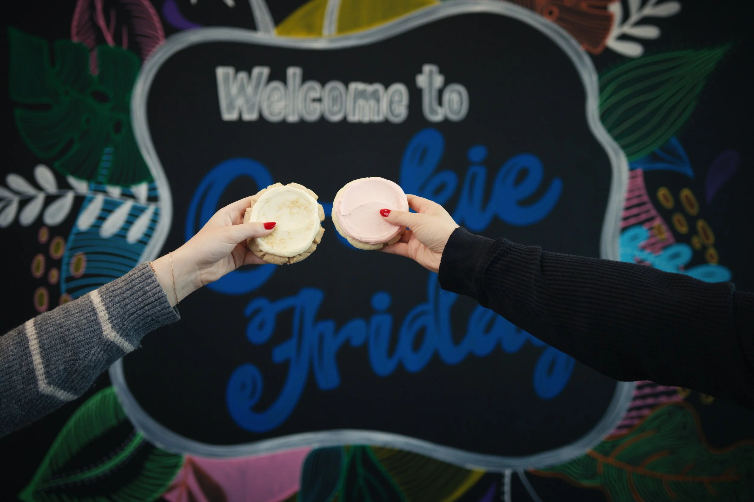 Two people holding ice cream sandwiches, one with vanilla and the other with pink ice cream, in front of a colorful 'Welcome to Oceanic' sign with tropical leaves and patterns.