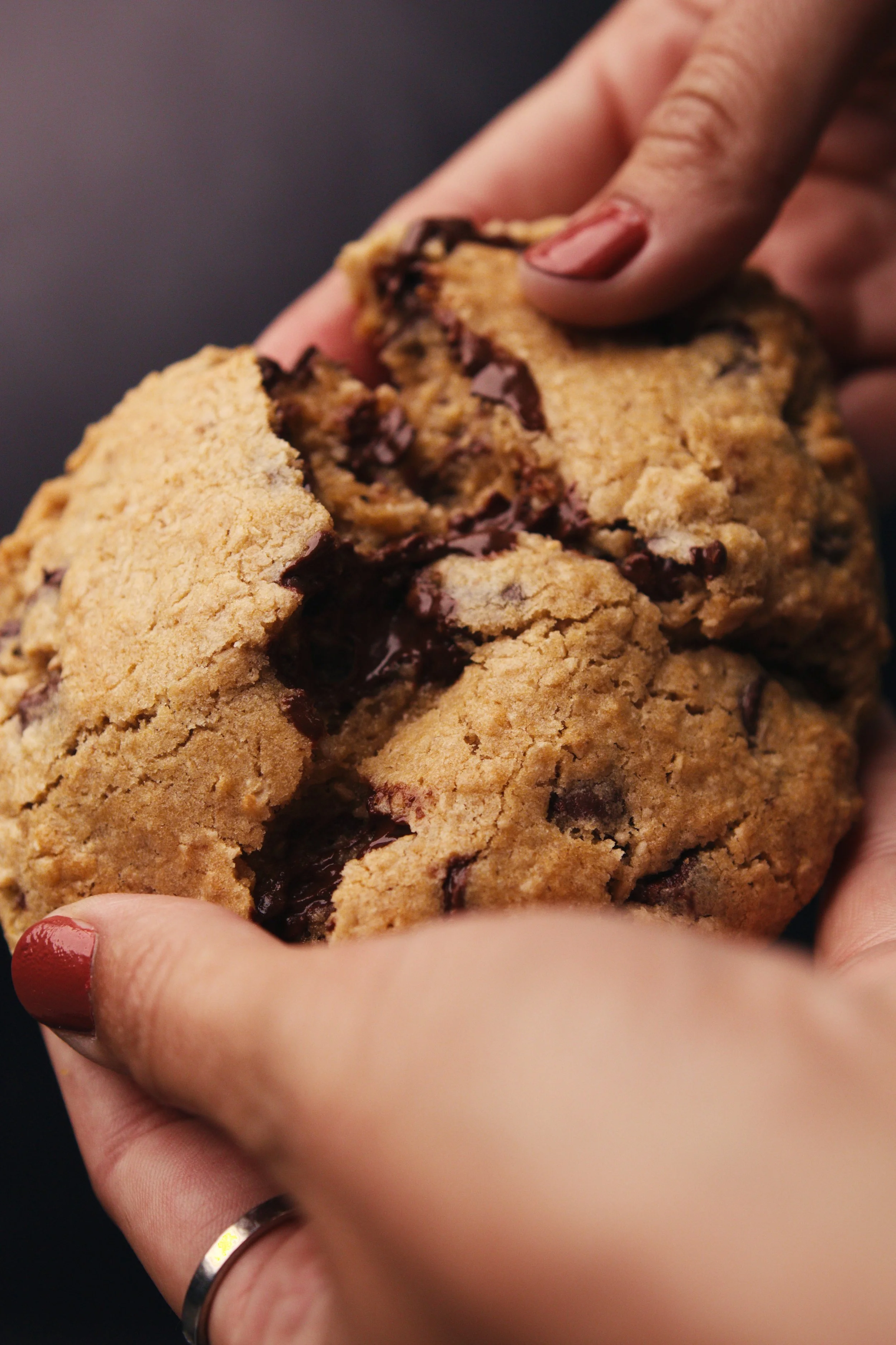 Close-up of a hand tearing a large chocolate chip cookie