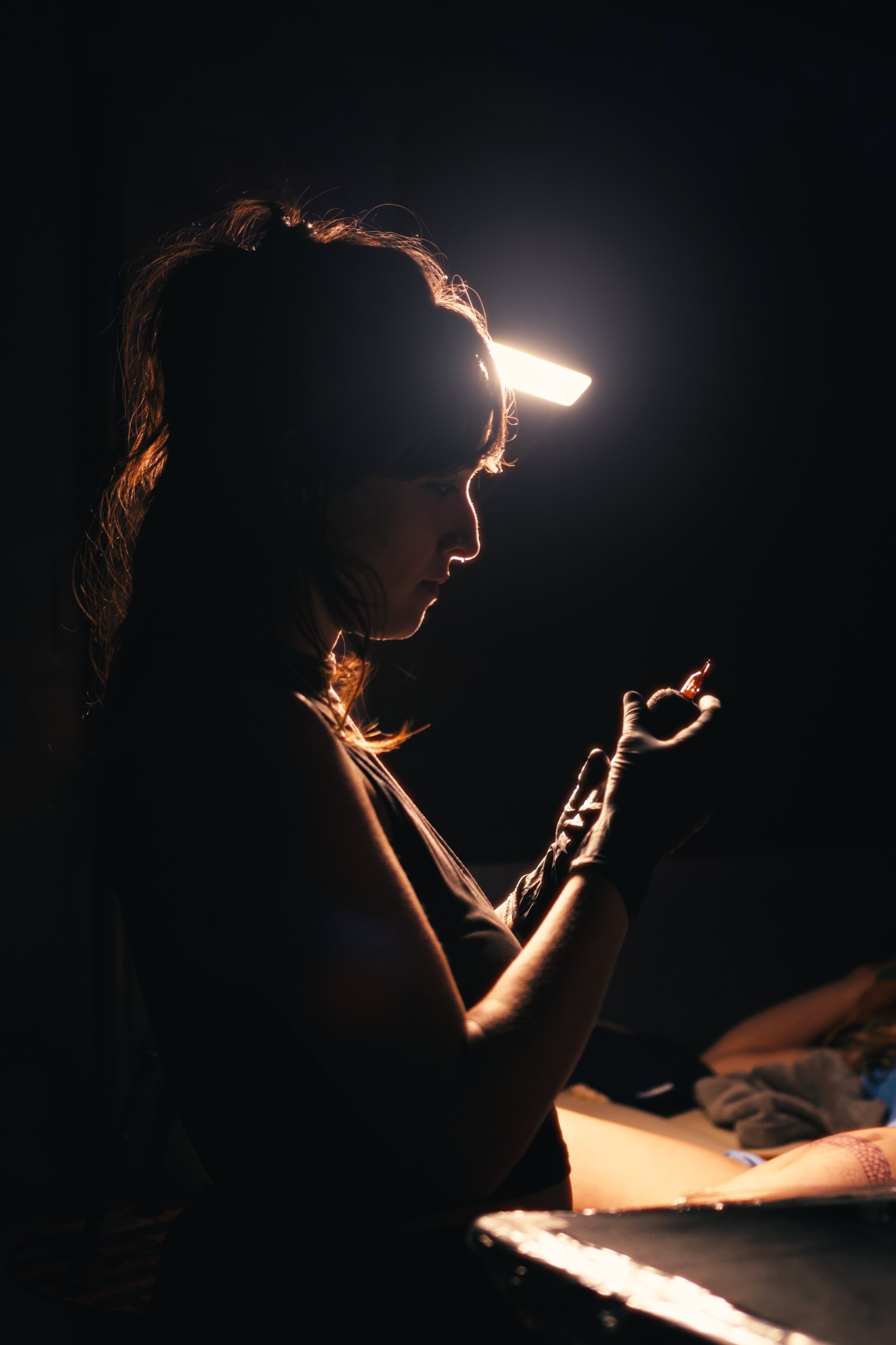 A silhouette of a woman with shoulder-length hair looking at her phone, illuminated by a bright light behind her, in a dark room.