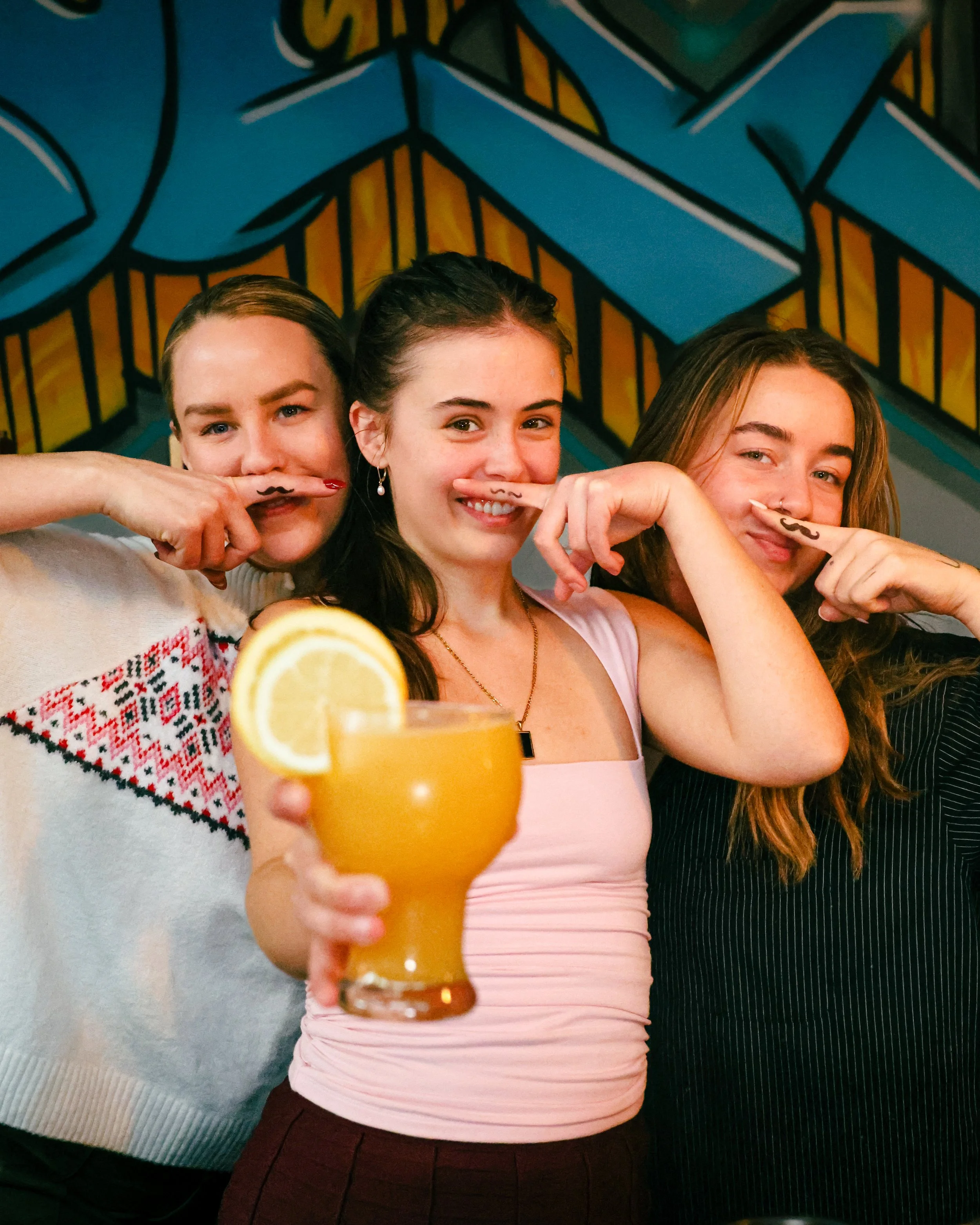 Three friends smiling and holding cocktails at Locus bar in downtown Bellingham