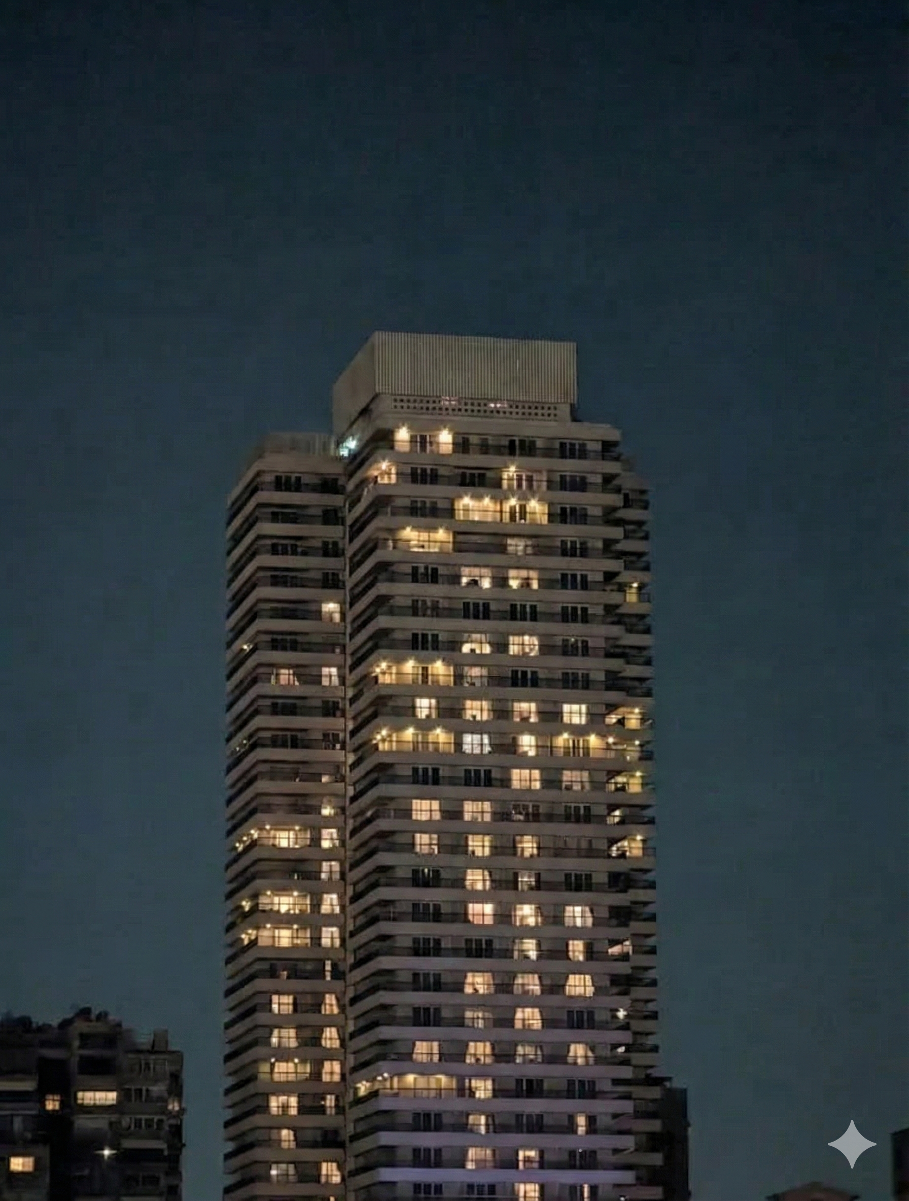 Tall residential building at night with multiple lit windows.