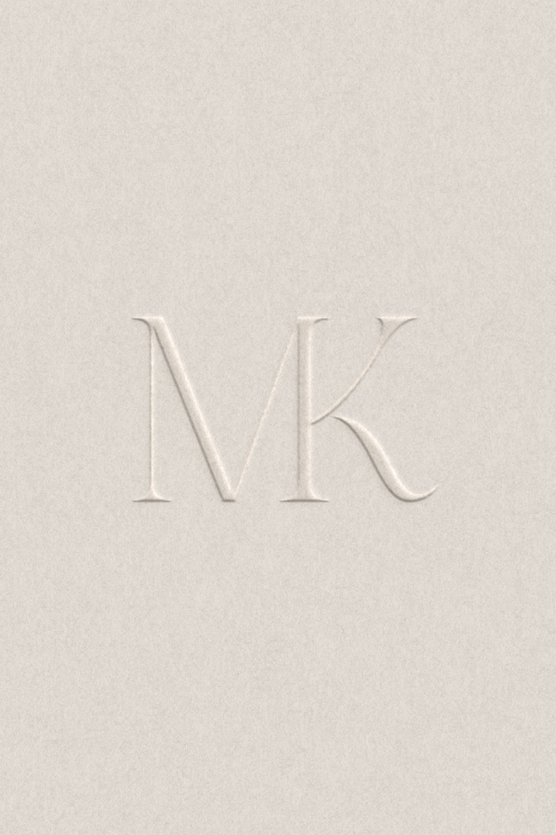 A beige textured surface with embossed MK initials for a custom couples monogram designed by our studio to complement our couple and complete their wedding stationary design.