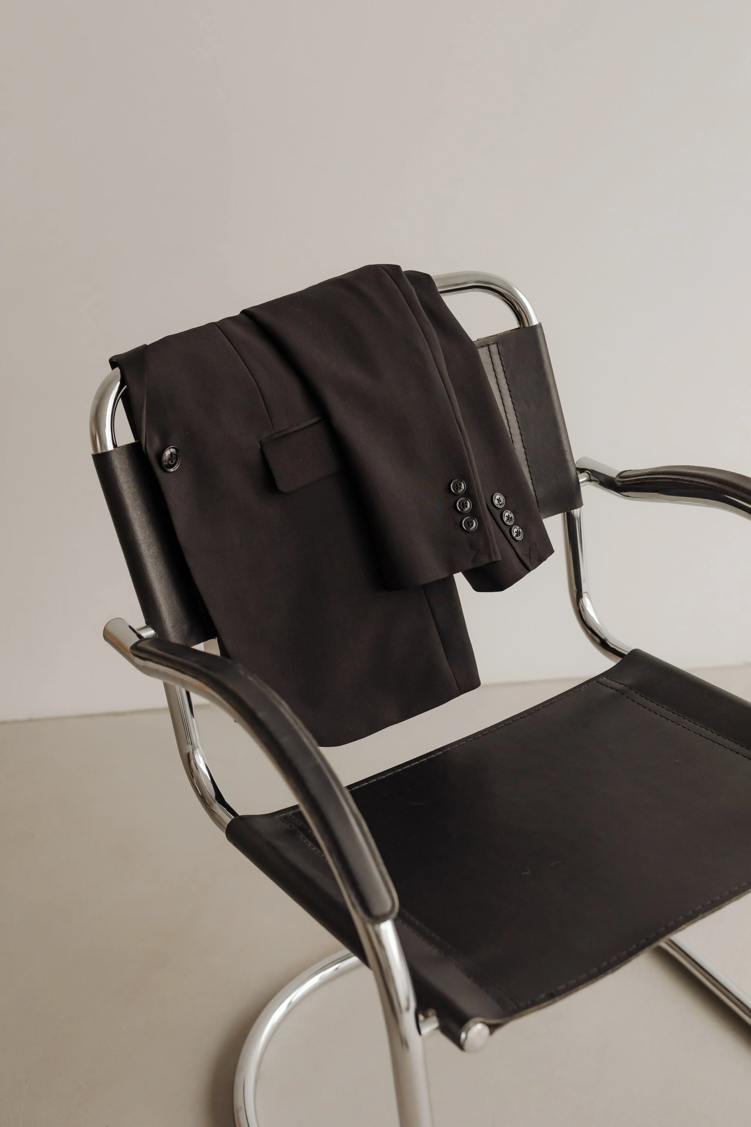 A black blazer draped over the back of a modern black leather and chrome chair