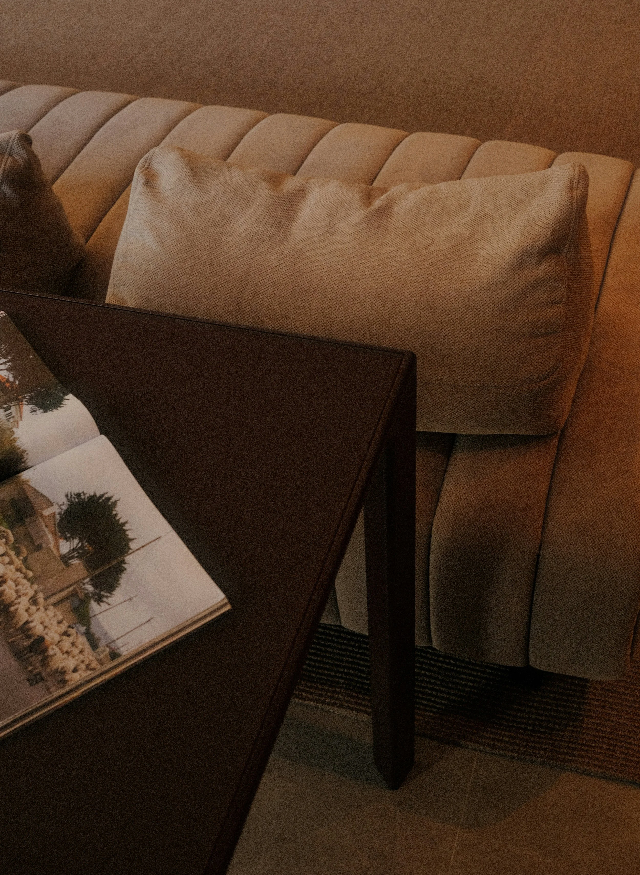Interior view showing a beige sofa with pillows and a dark wooden table with a photo album on it.