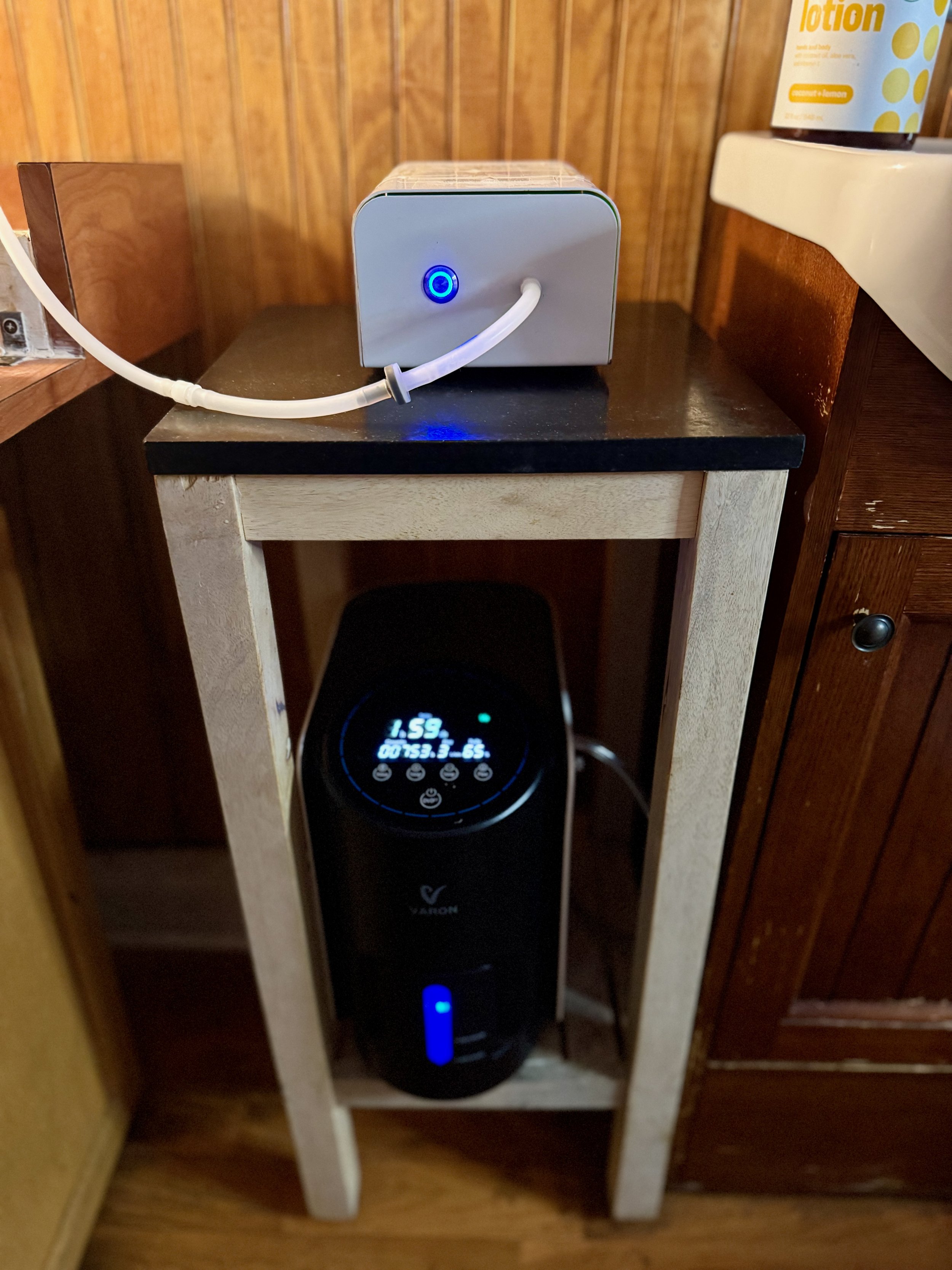 A humidifier on a small wooden stand with digital display and control buttons, next to a black appliance, in a room with wood-paneled walls.