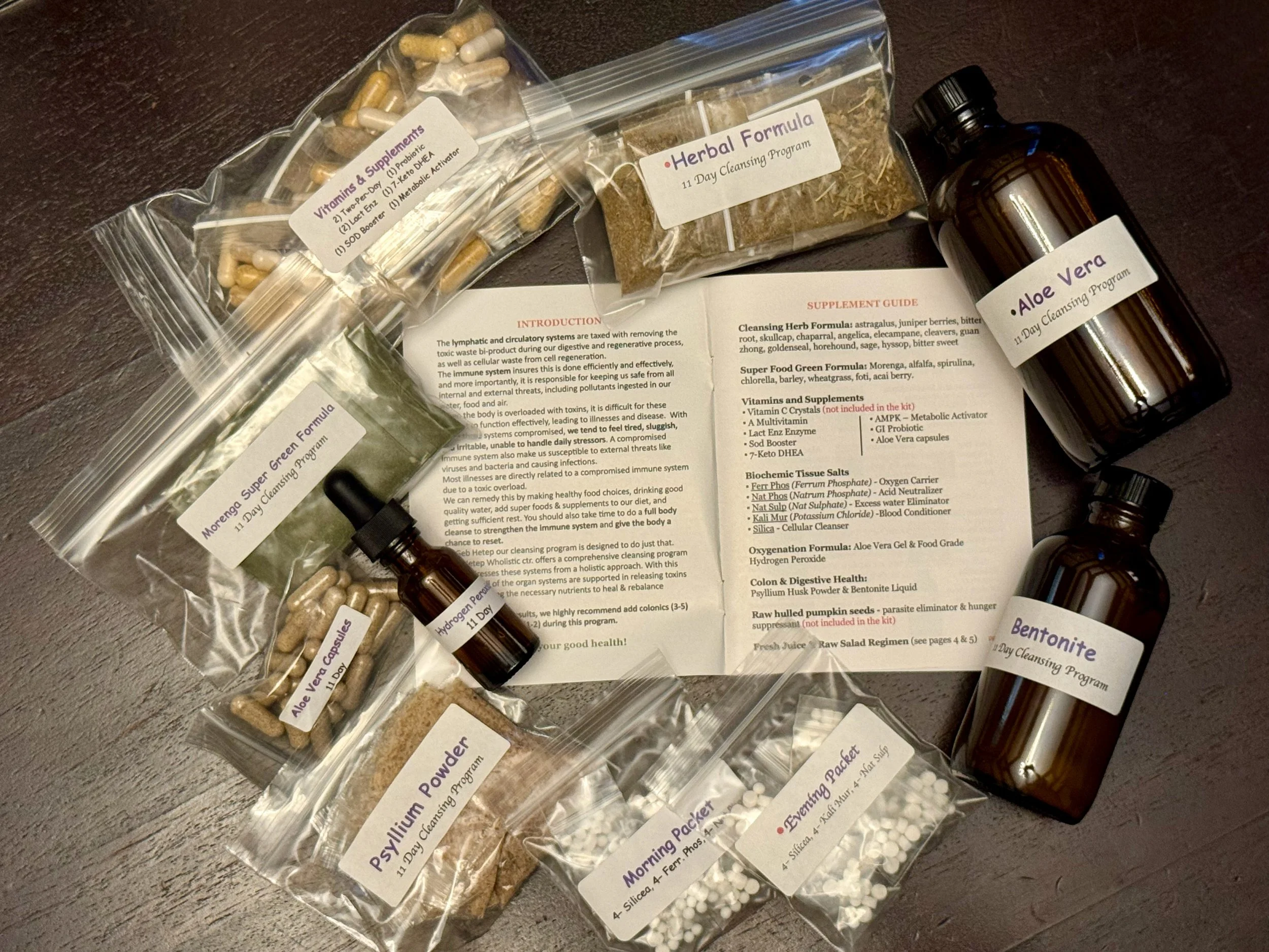 Collection of bottles, packets, and capsules for a 11-day cleansing program, including herbal, aloe vera, bentonite, and other detox supplements with an instruction sheet.