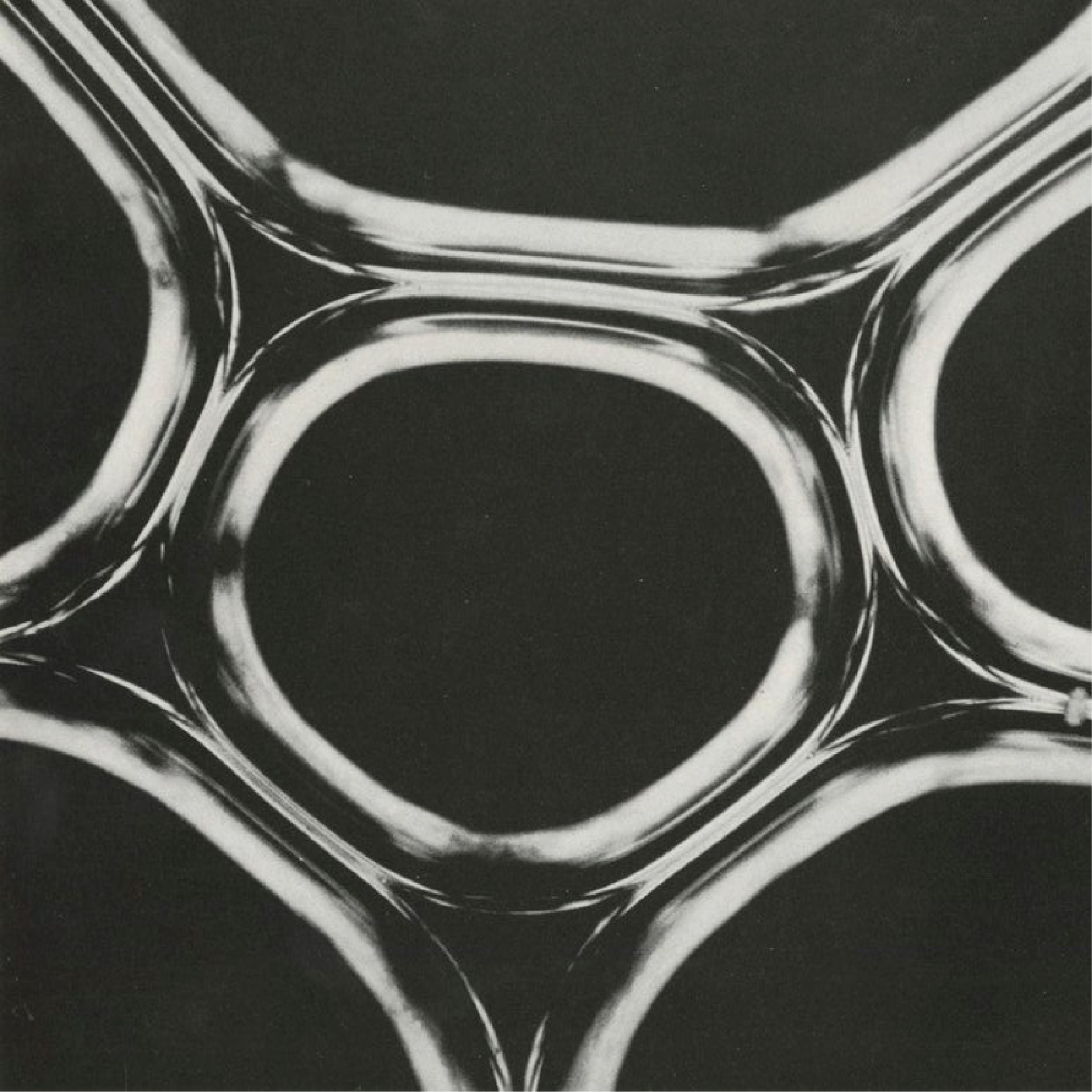 Close-up black-and-white photograph of multiple glass tubes or pipes arranged in a geometric pattern.