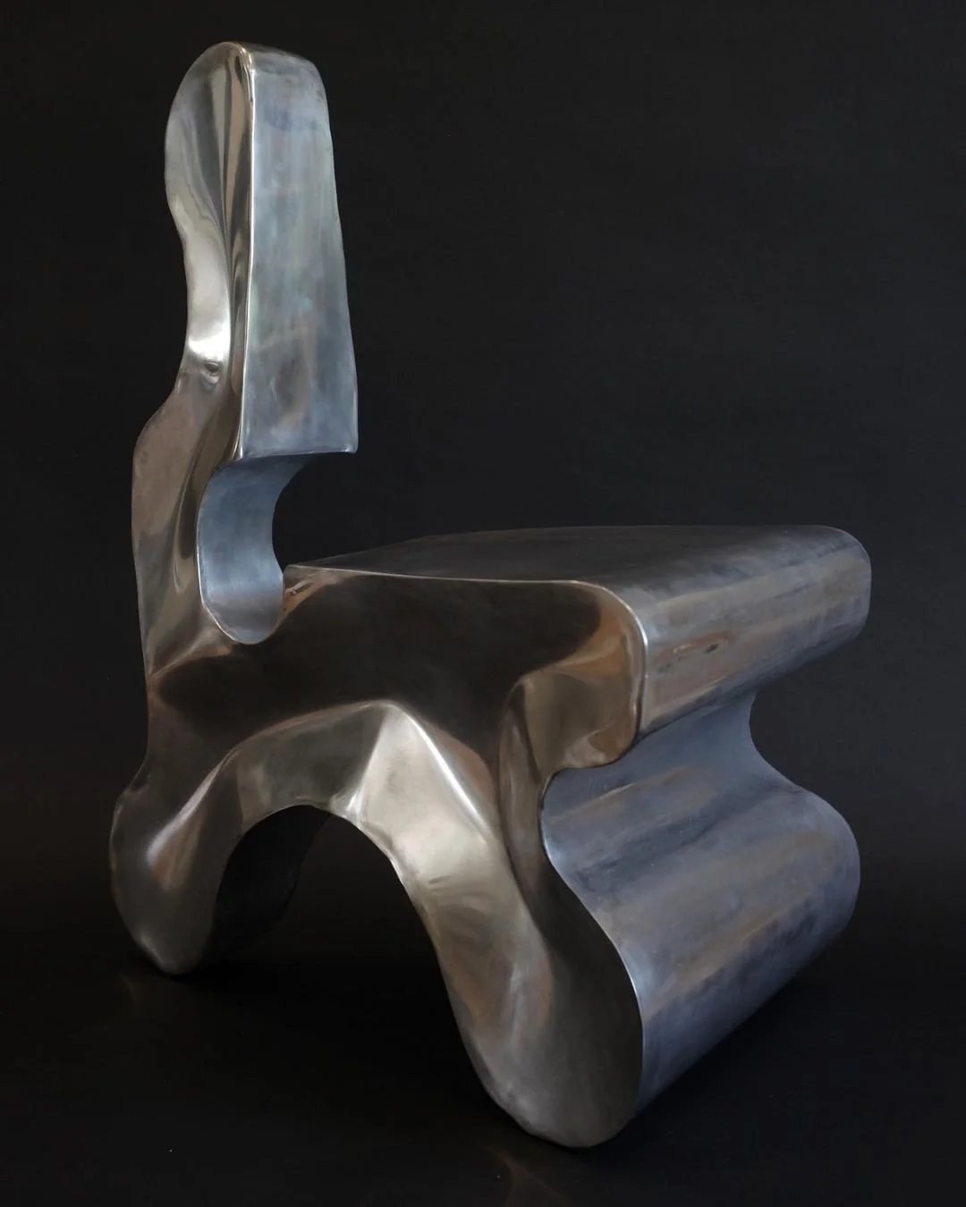 Modern metallic chair with an abstract, sculptural design against a black background.