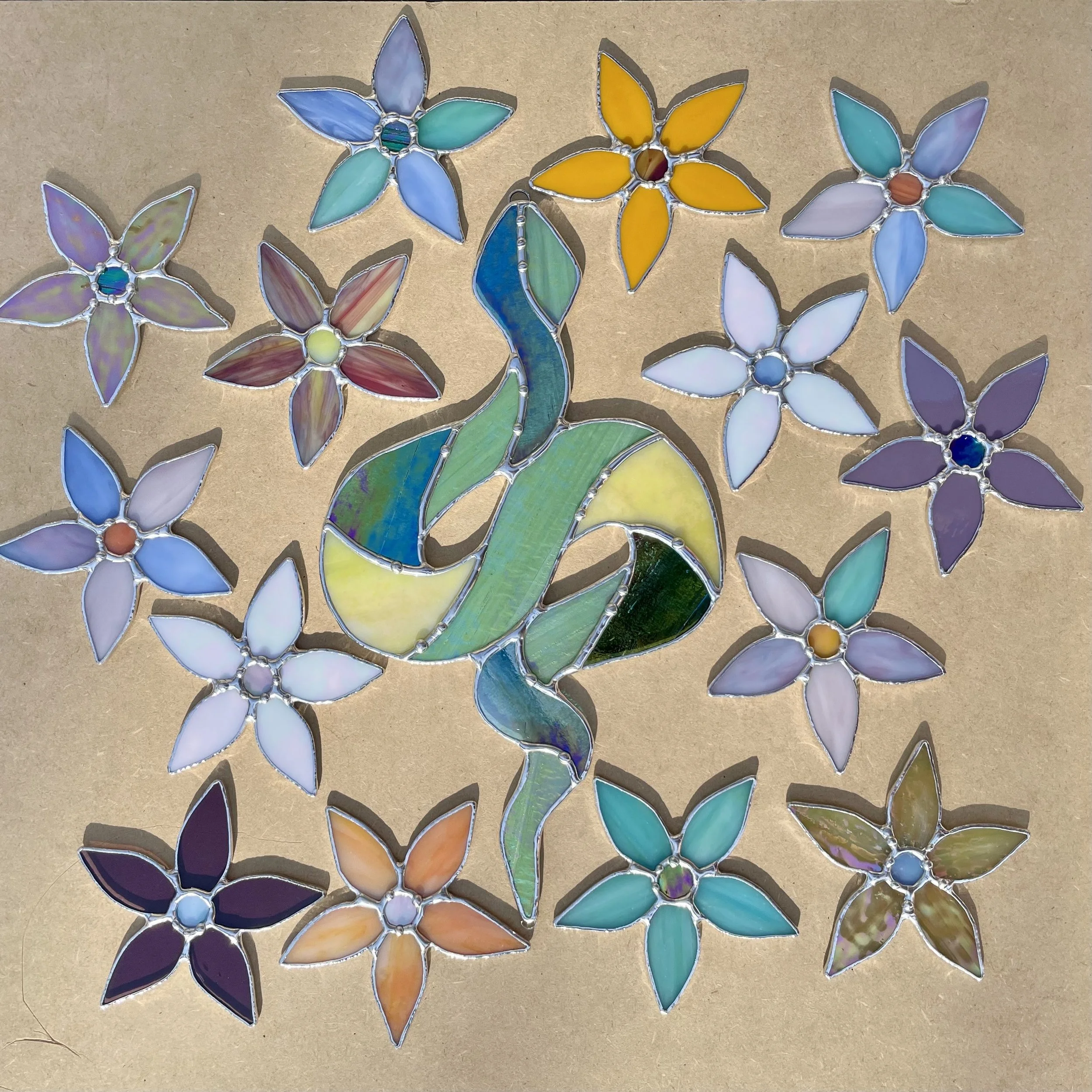 Colorful stained glass art featuring a flamingo surrounded by floral designs on a tan background.